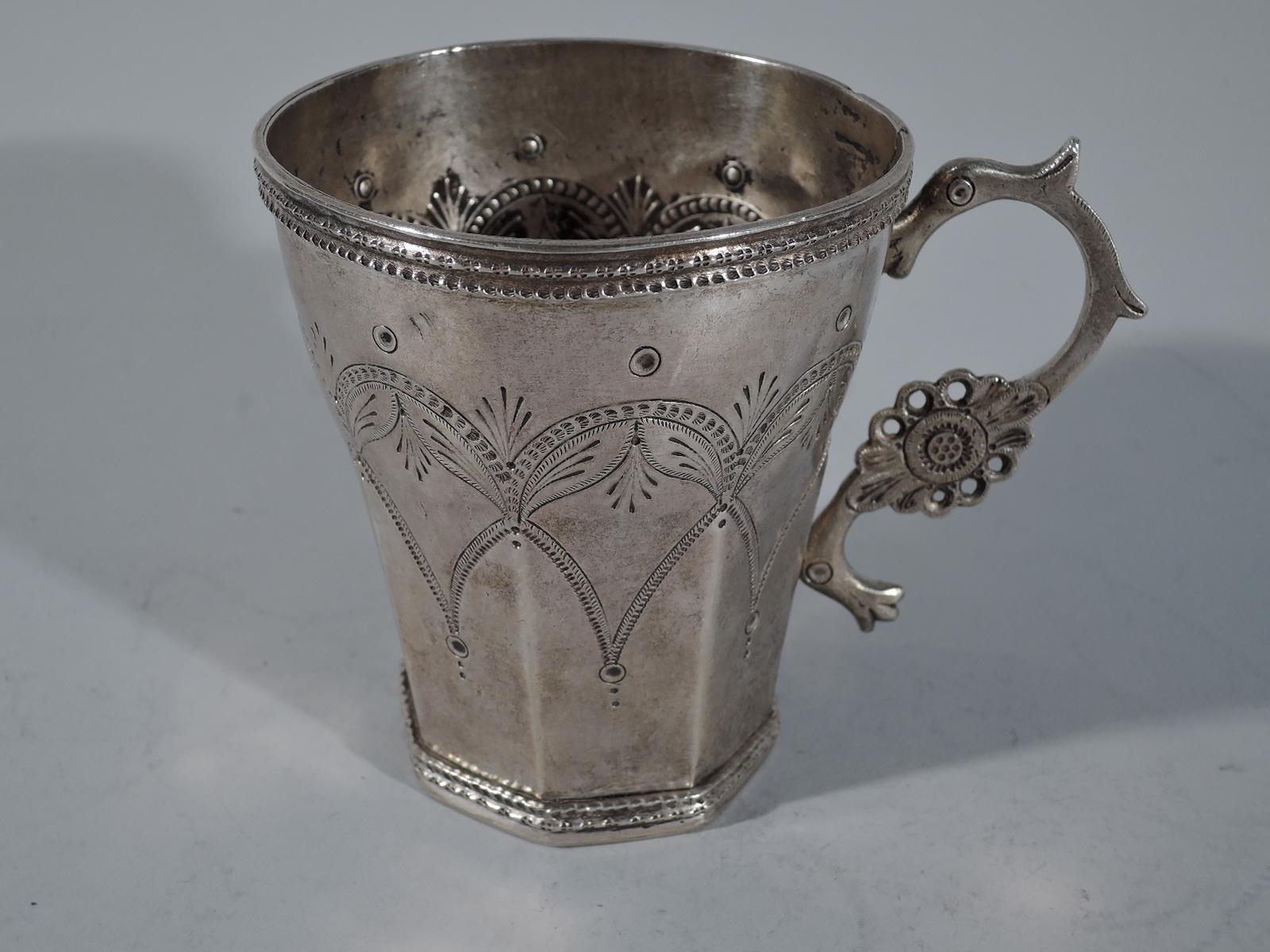 Large South American silver mug, 19th century. Curved top and faceted bottom with tooled double arcade border interspersed with stylized leaves. Pointille rim borders. Naive animal-form handle with pierced flower head. Shaded initials JC on