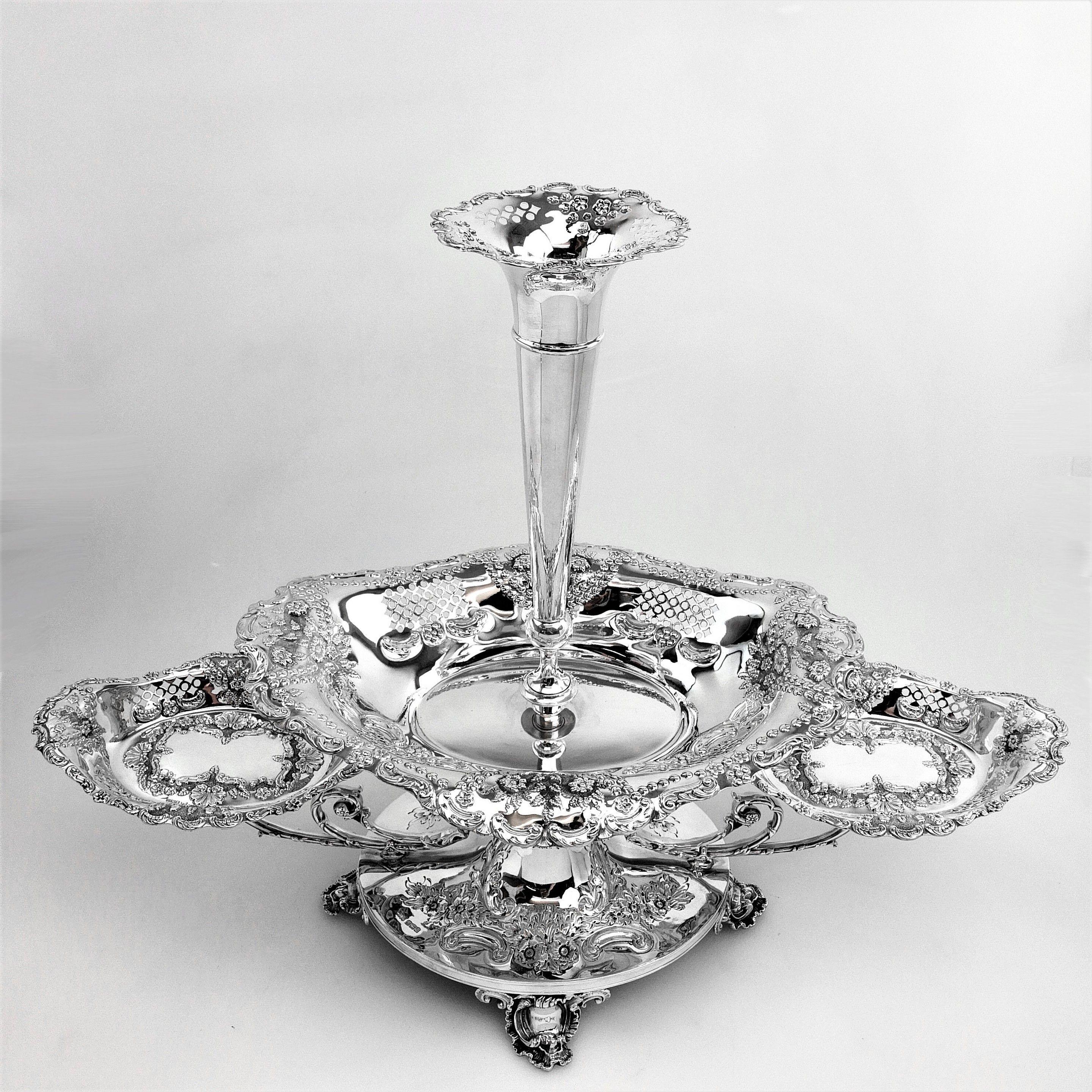 A magnificent antique solid silver epergne centre piece to ornament any table. Standing on an impressive oval pedestal base supported by four ornate feet, the epergne has a large oval central basket and two smaller oval baskets extending out on