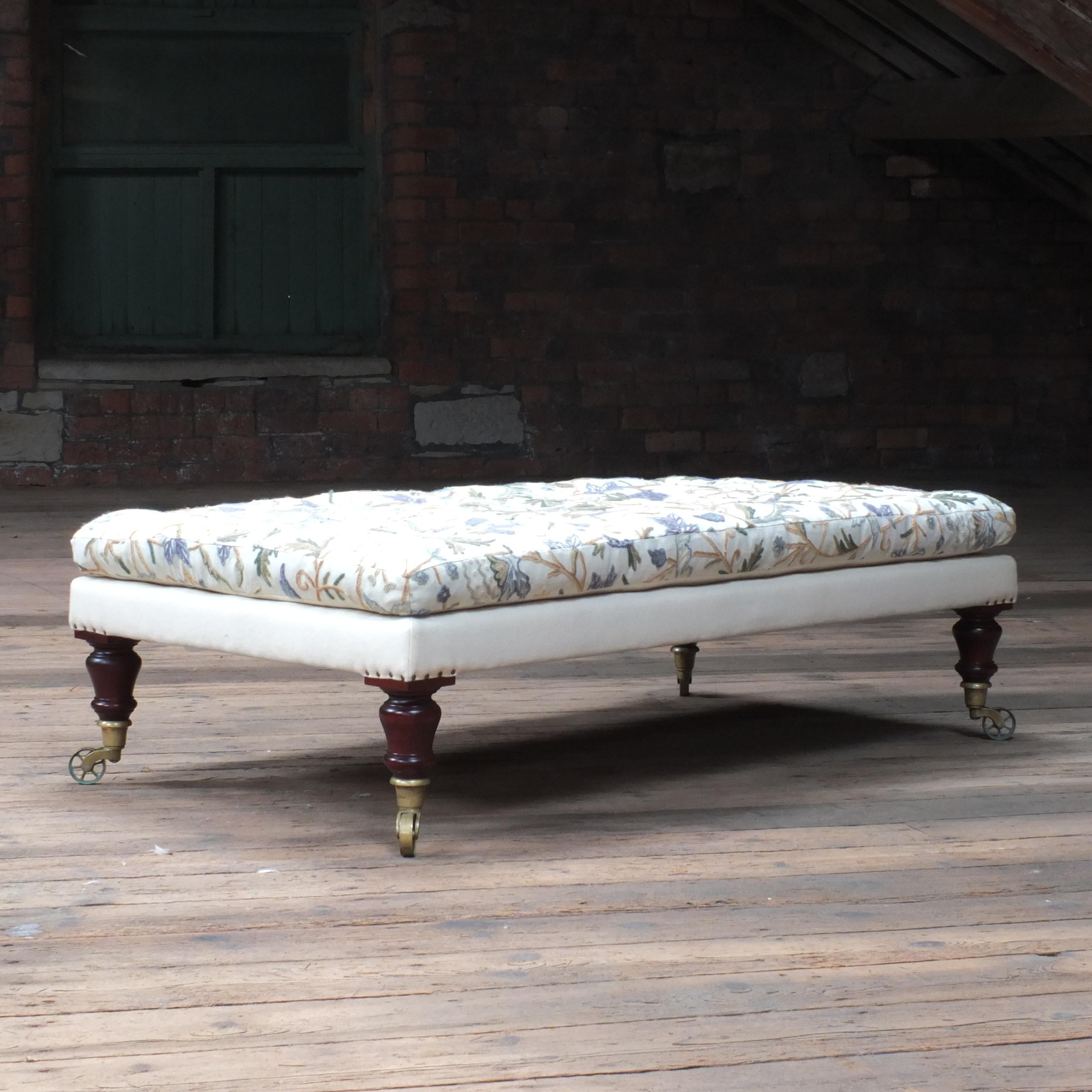 A large bespoke country house footstool. Upholstered in a vintage Indian crewel work top and an off white wool base. Raised on 4 hand turned Brazilian mahogany legs with rosewood stain and all finished with early 19th century Lewty lost wax castors.
