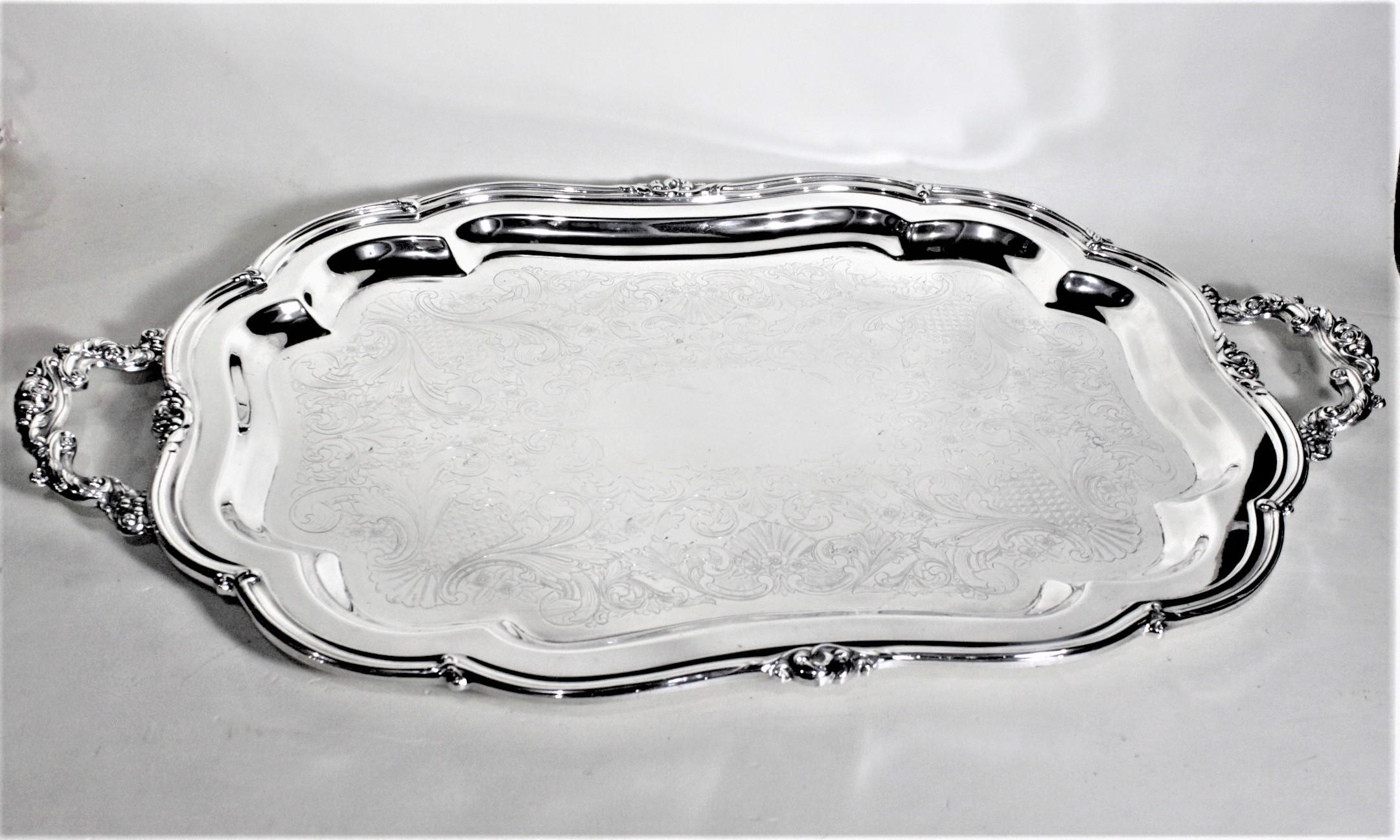 This vintage and very large rectangular silver plated serving tray was made by Community plate of the United States in approximately 1960 in an English Victorian style. The tray has a tiered scalloped rim with accenting decoration on either side,