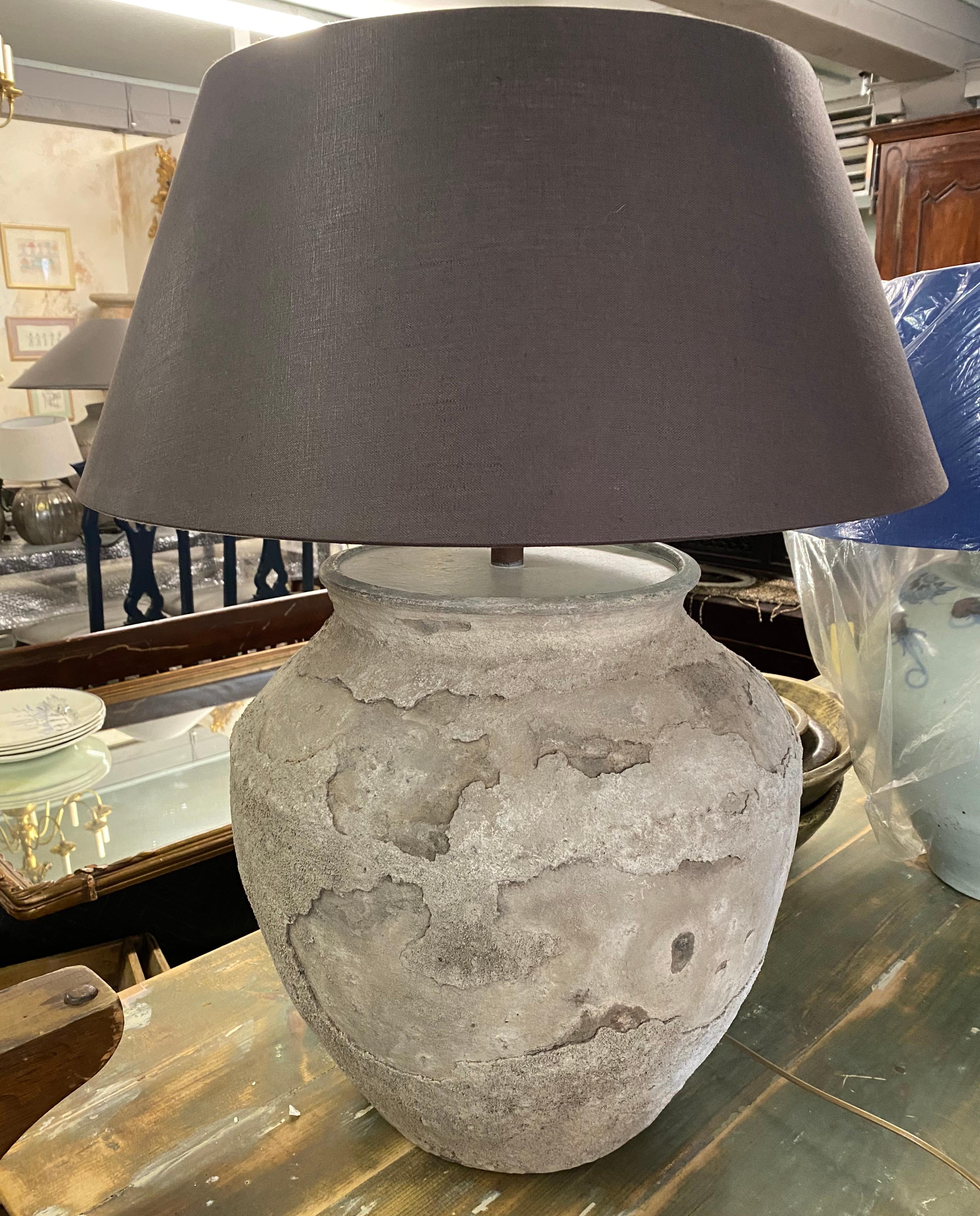 Impressive large rustic organic Chinese unglazed terracotta storage jar that has been made into a table lamp. The vase has beautiful aged patina from being buried perhaps for centuries. Handmade drum shape Belgium linen lampshade included.
 
