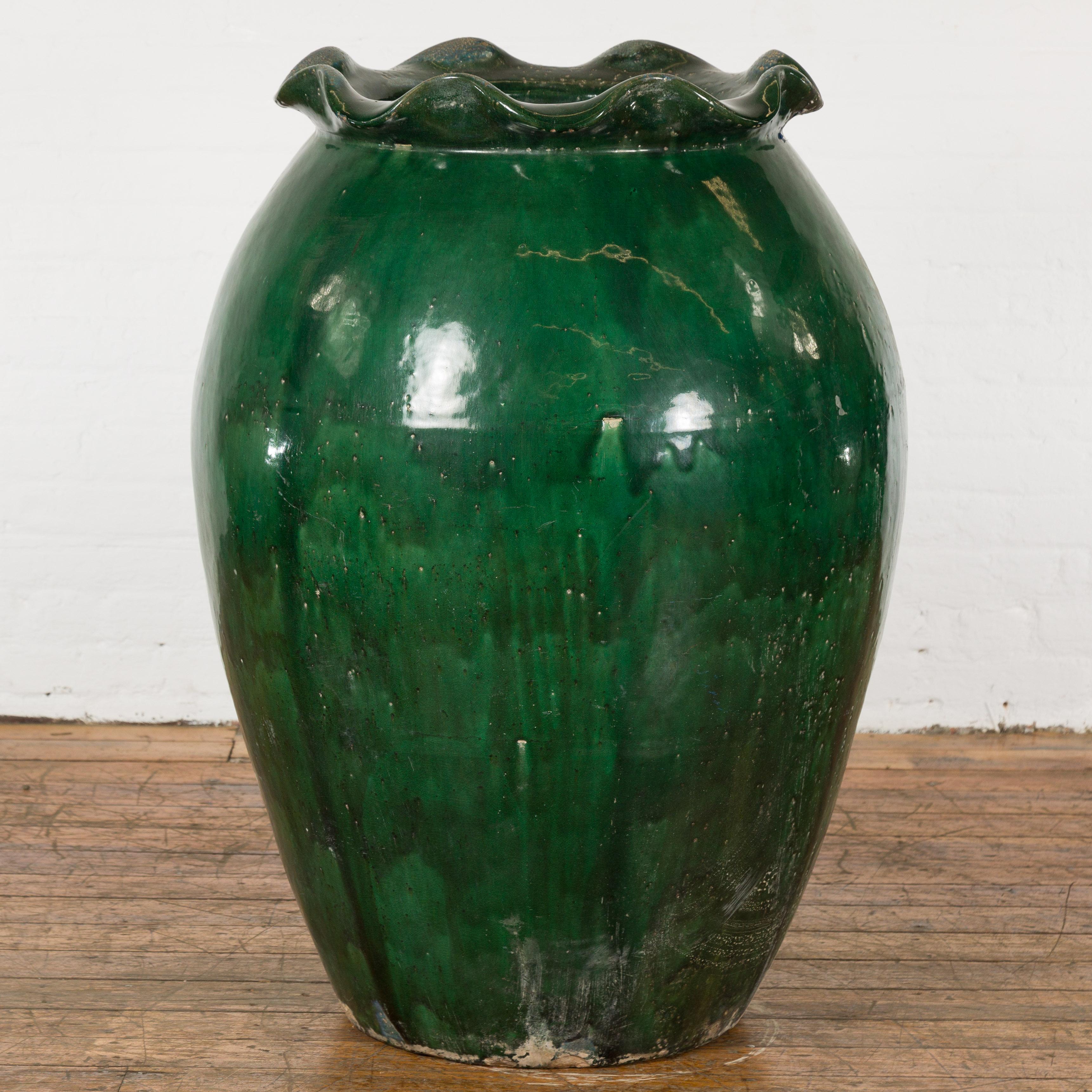 A large antique Thai ceramic planter from the 19th century, with green glazed finish, scalloped lip and weathered patina. Created in Thailand during the 19th century, this planter attracts the attention with its oversized silhouette and distressed