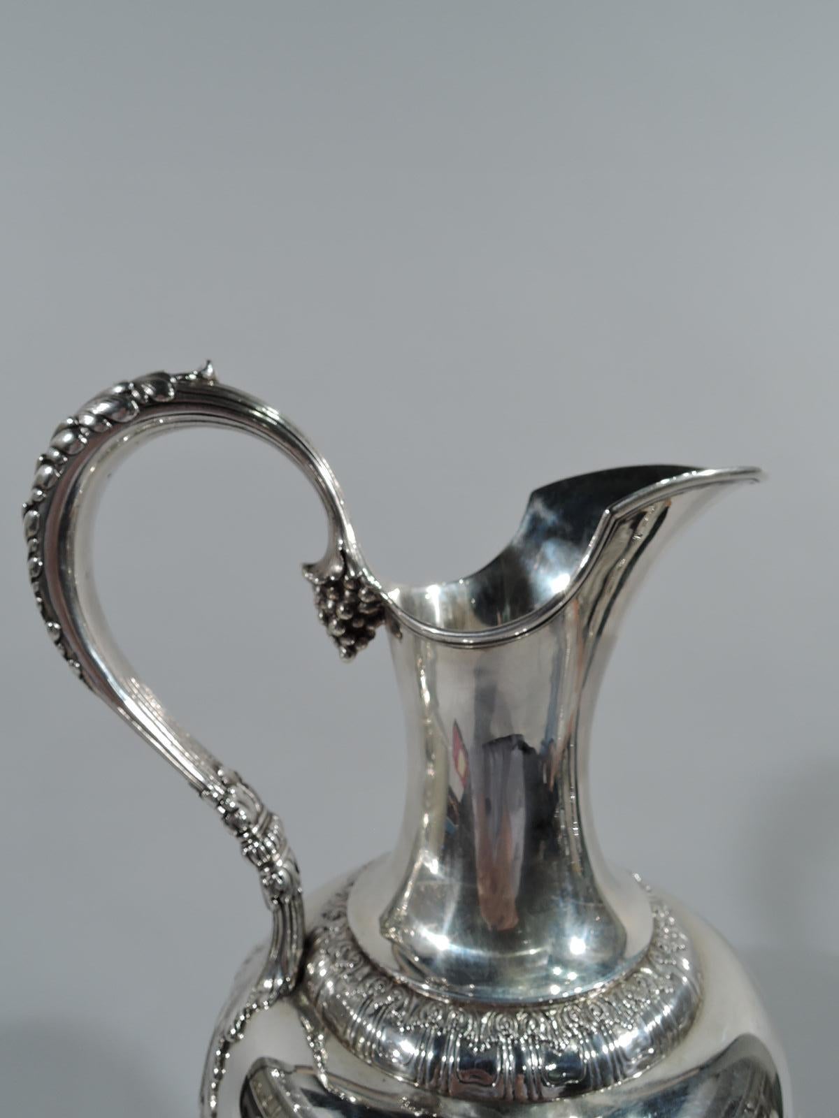 Neoclassical sterling silver ewer. Made by Tiffany in New York. Ovoid body, helmet mouth and spout, leaf-mounted and capped reeded scroll handle with grape-bunch terminal, short flanged stem, and domed foot. Body encircled with military frieze