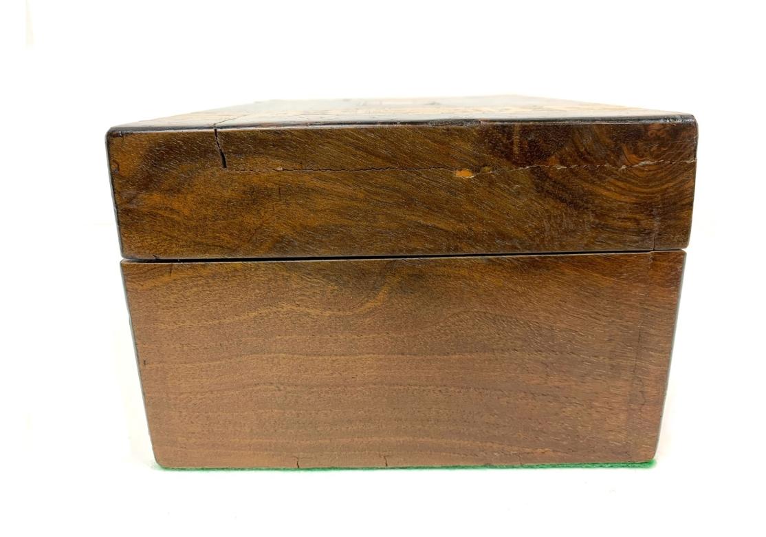 Gran caja antigua de Tunbridge Ware con una ancha banda geométrica incrustada en la parte superior y frontal. La tapa y el escudo tienen un medallón rectangular incrustado. La tapa abatible se abre para revelar un interior forrado de papel. El fondo