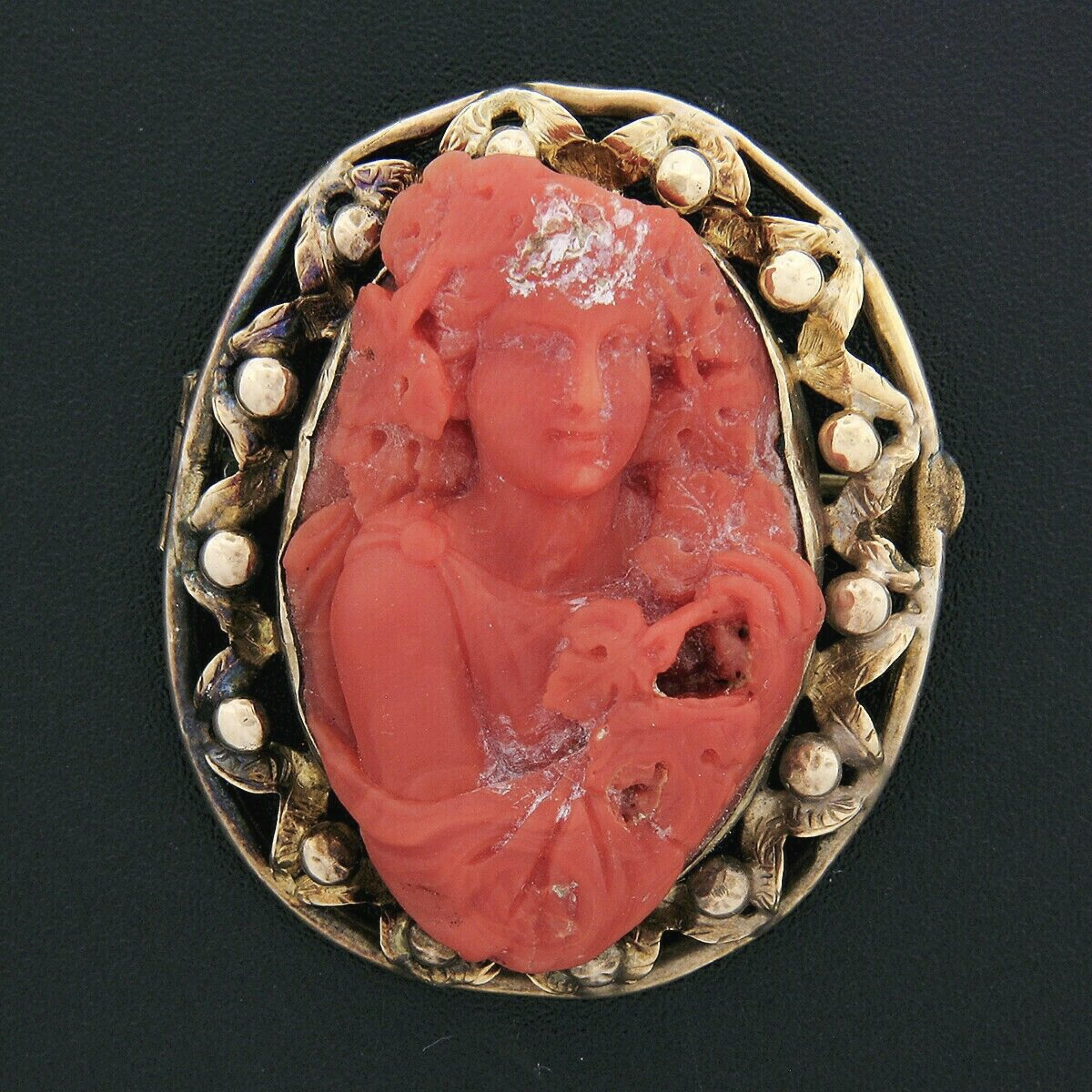 This large handmade antique brooch was crafted in solid 14k yellow gold during the Victorian era. It features a GIA certified, natural coral stone set into an open work and hand etched floral themed frame. The coral is a rich orange-red color and is