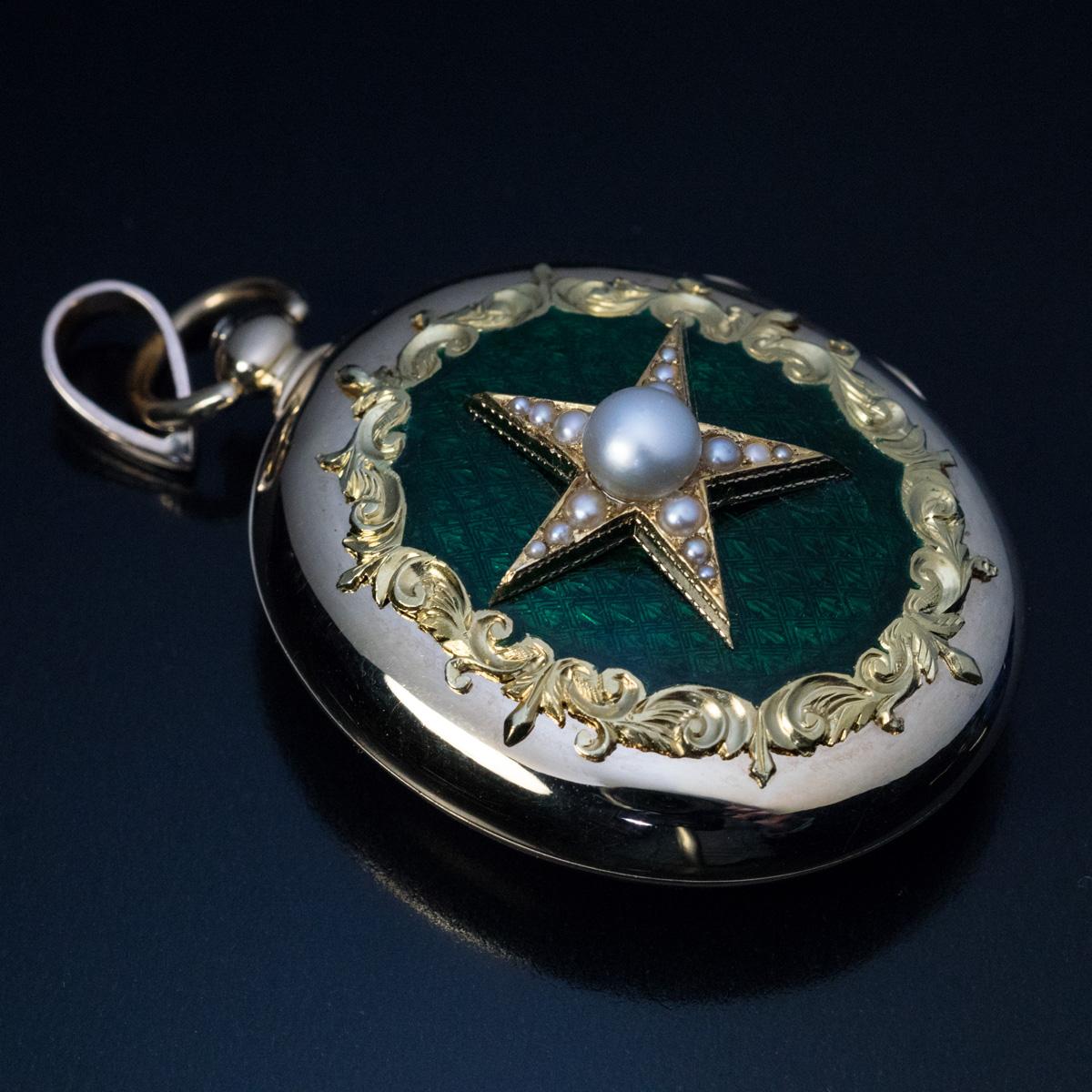 Austrian, circa 1870

An impressive antique Victorian era large locket pendant is finely crafted in two tone 14K gold. The front cover of the locket is centered with a pearl star mounted on an alpine green guilloche enamel background and surrounded