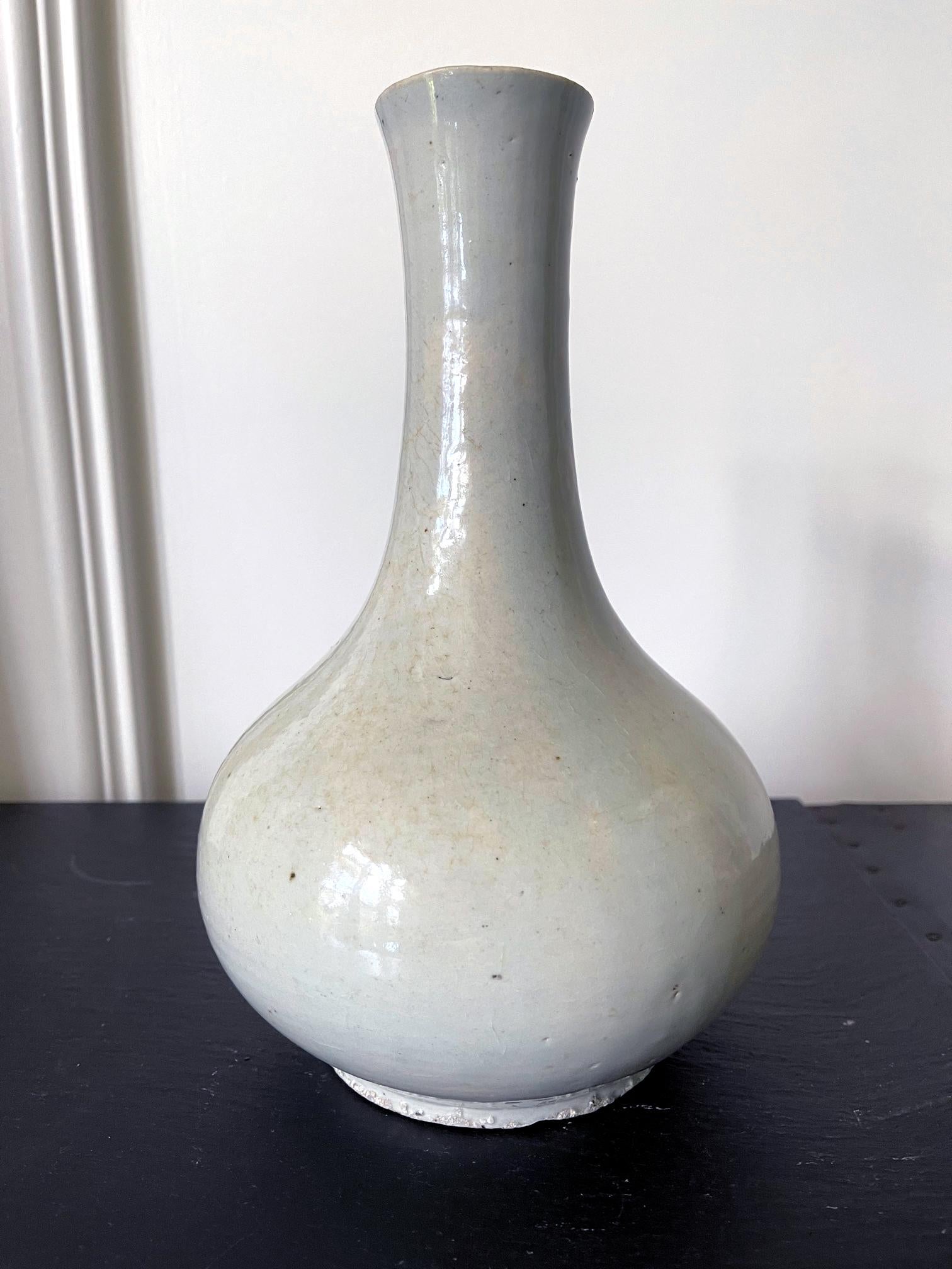 On offer is a Korean ceramic bottle vase circa 19th century made in the late Joseon dynasty (1392-1910). The vase is of a classic bottle form with a bulbous body and a long neck with a slightly rolled mouth rum. The all over glaze is white with a