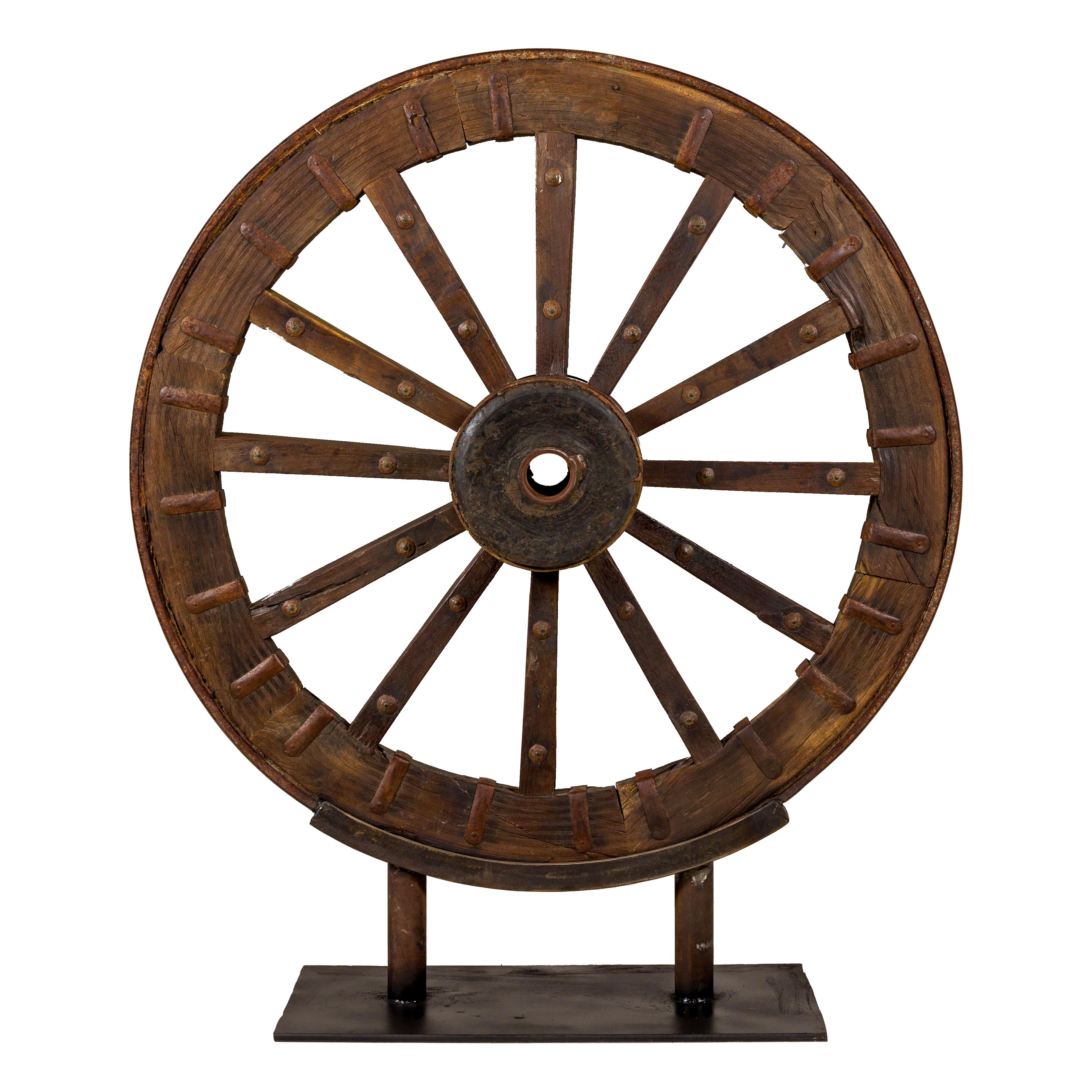 An antique Indian wood and metal cart wheel mounted on custom black metal base. Introduce a touch of rustic authenticity to your living space with this exquisite antique Indian cart wheel, an object d'art that marries vintage charm with contemporary