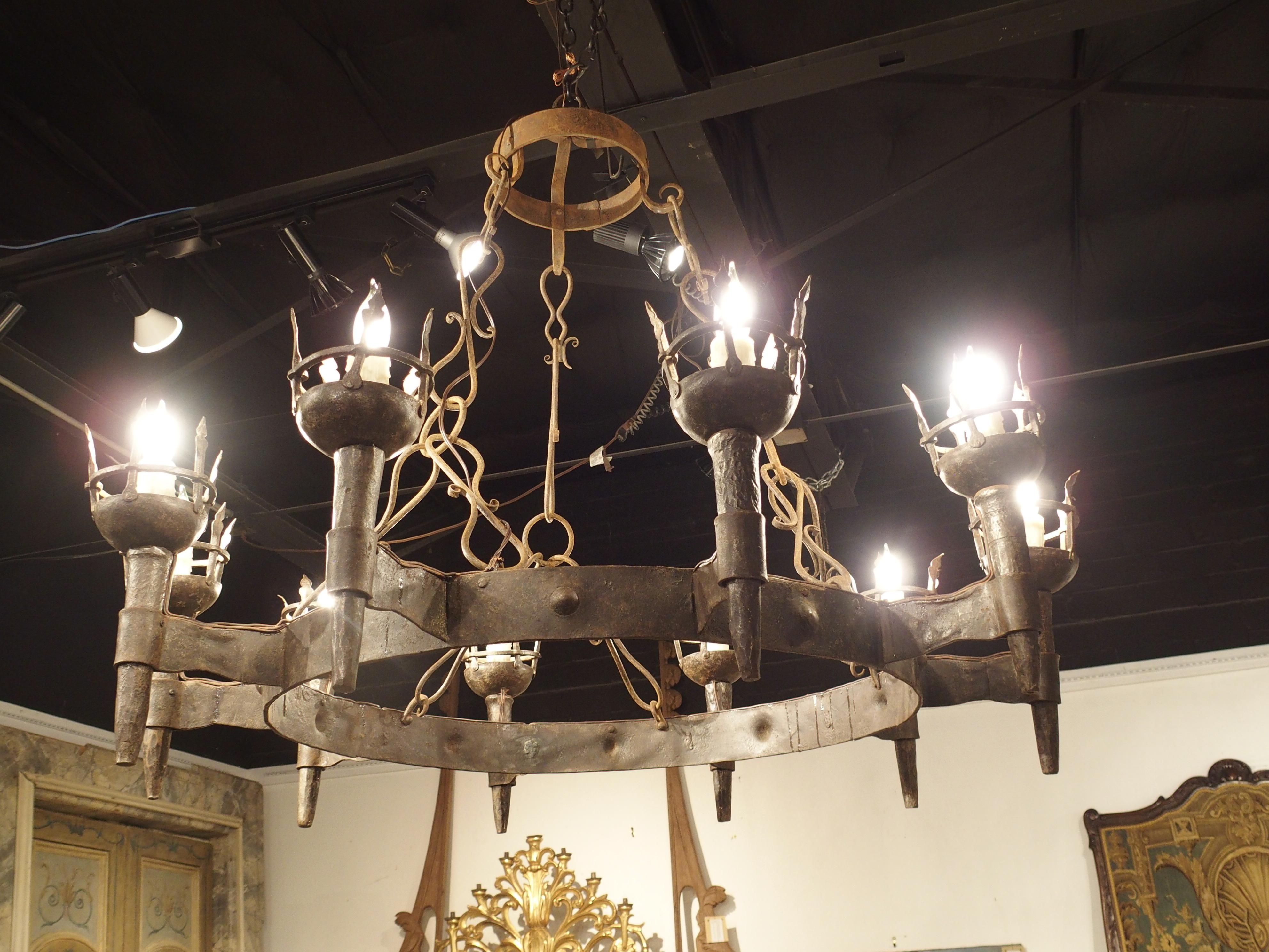 An exquisite and large light source, this hand wrought iron torch chandelier hails from the late 1800s. Crafted in France, the chandelier boasts a captivating design featuring hand-hammered roundels adorning the open ring that gracefully cradles ten