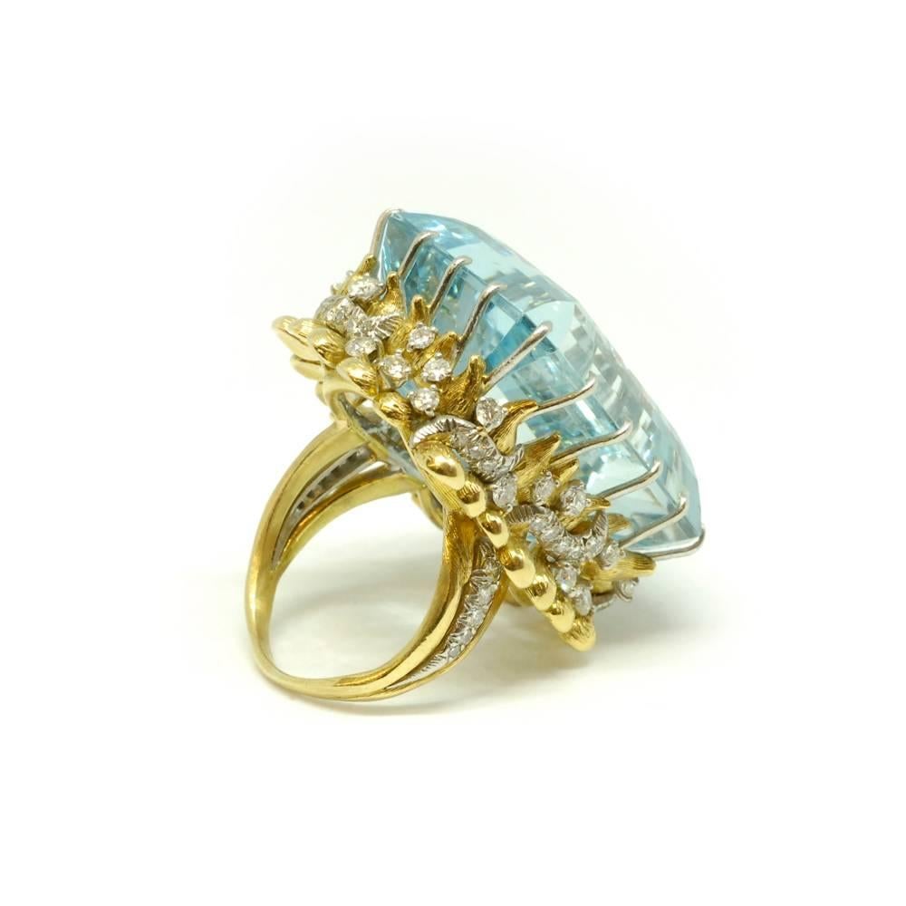 A large aquamarine cocktail ring with textured gold ‘tendril’ mount, set with diamonds. American, circa 1940.The aqua weighs approximately 60ct.