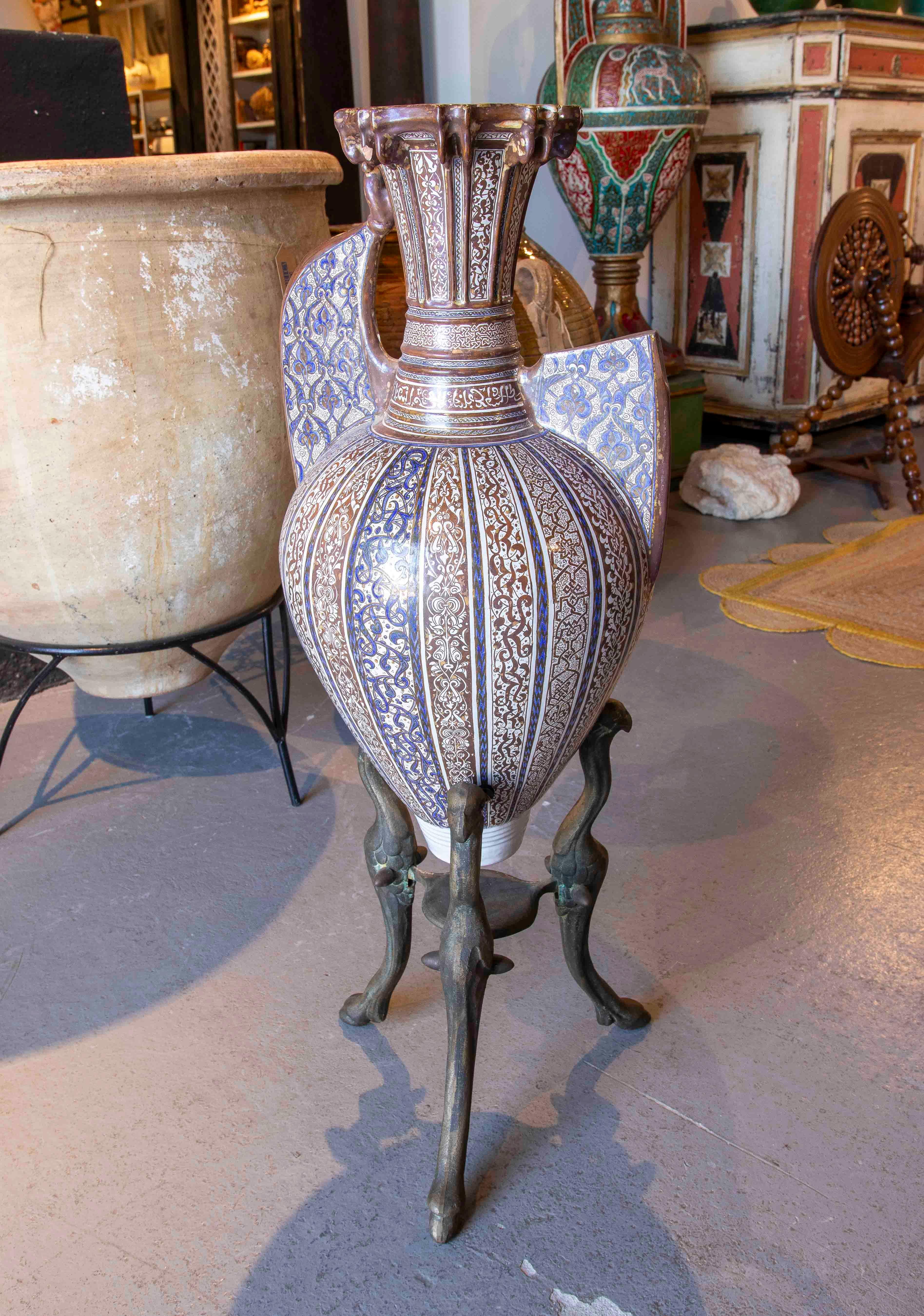 Impressive Arabic-inspired jar made of glazed ceramic with rich calligraphic and geometric motifs in cobalt blue and brown on a white background. The piece is topped with an ornate lid and rests on an elegant wrought iron tripod with zoomorphic