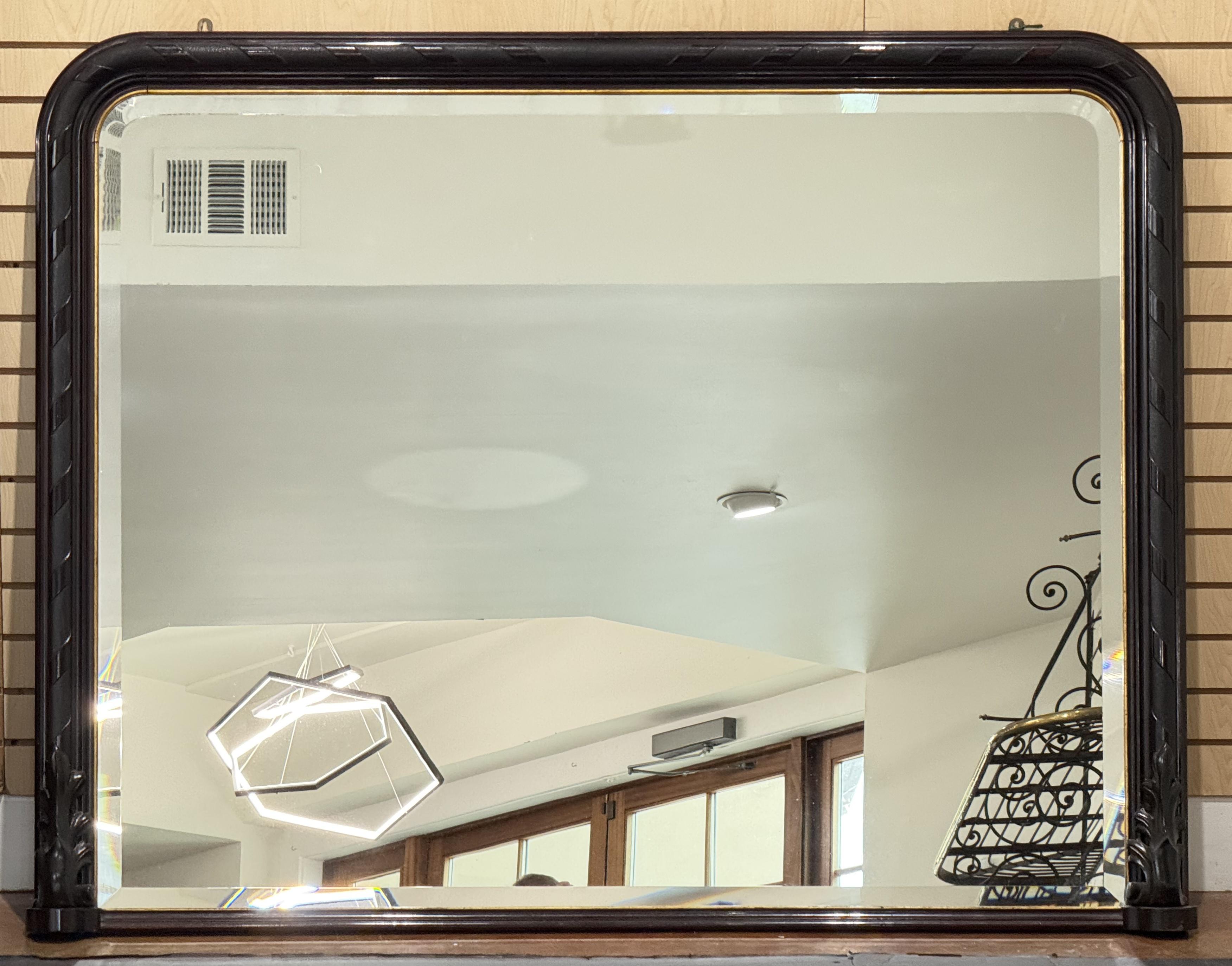 A fine large French rectangular arch top wall or hall mantle mirror from the 19th century, featuring a moulded surround of ebonized wood with gilt accents around a beveled glass mirror, and beautifully carved acanthus leaves on opposing ends of the