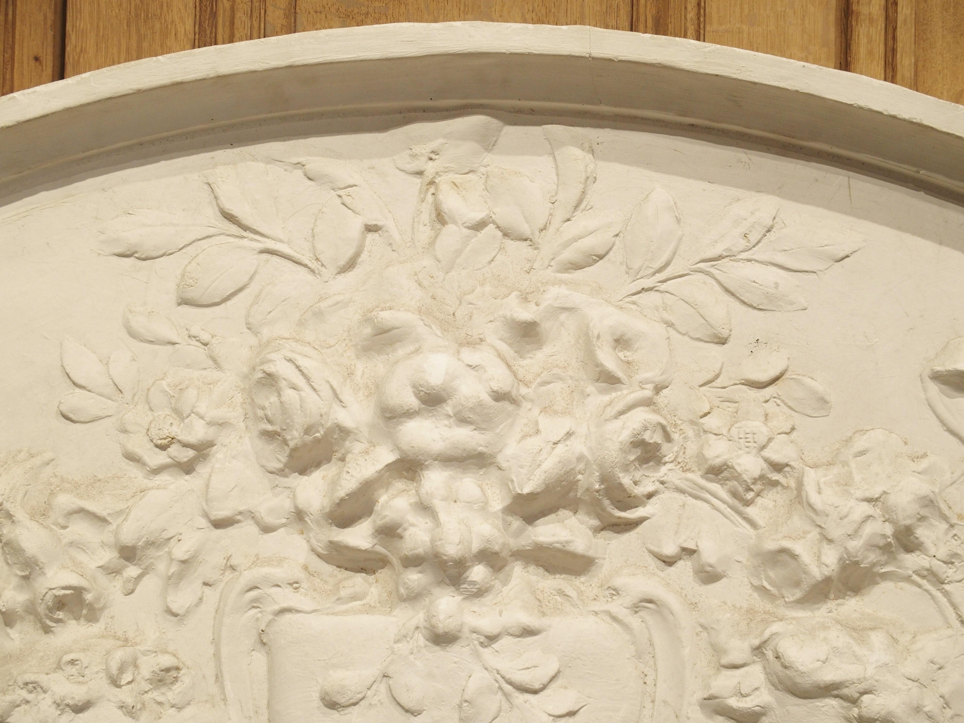 Produced in France, this large arched plaster overdoor has been sculpted in bas-relief, or low relief. In bas-relief, a sculptural image is raised to a shallow depth above the background. If viewed from the side, the sculpture has no meaning, as
