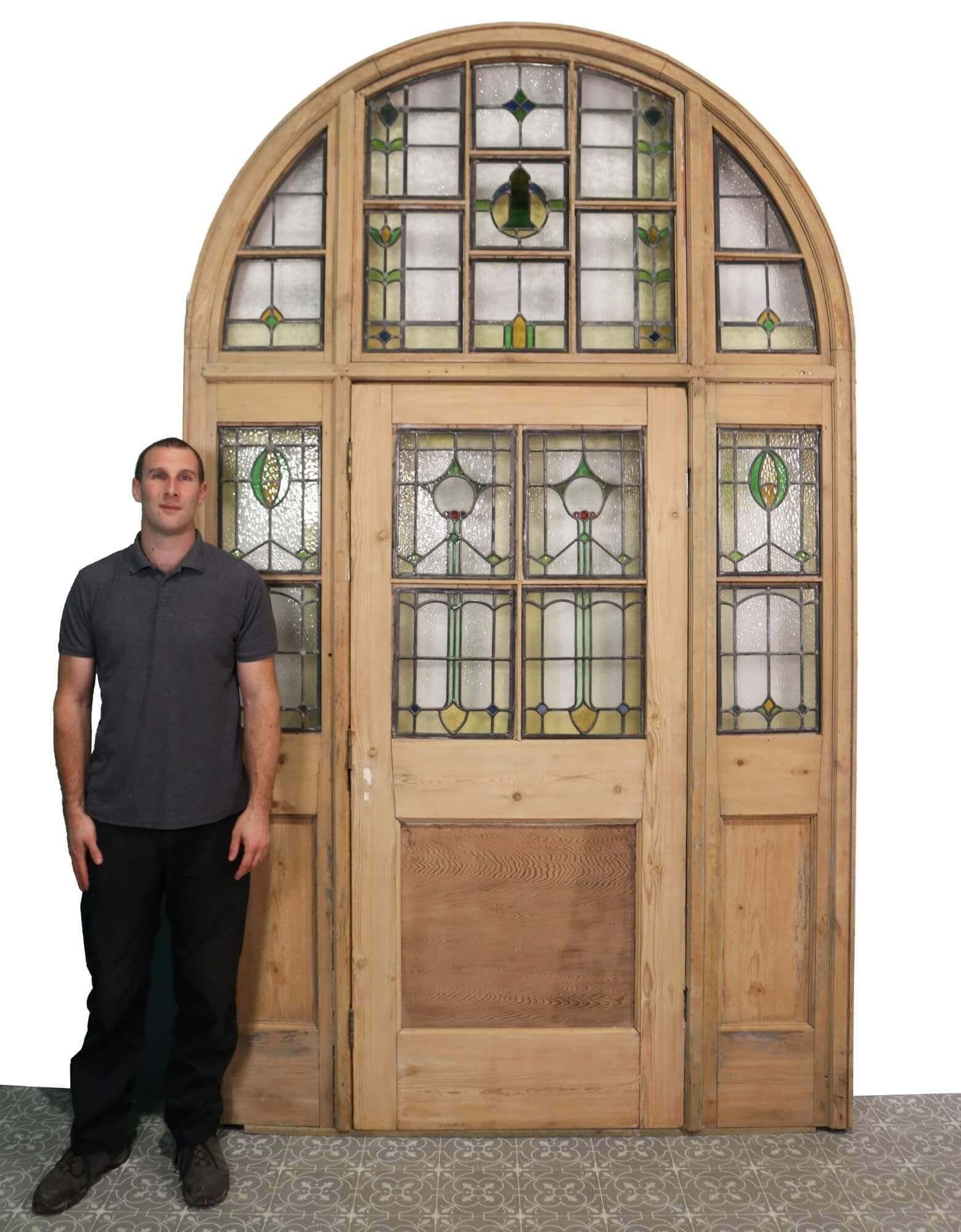 This impressive reclaimed stained glass door with frame provides a stunning entry to a property. Made up of an antique pine door within fixed side panels beneath a glazed arched demilune top, it is a rare find and in beautiful condition, having