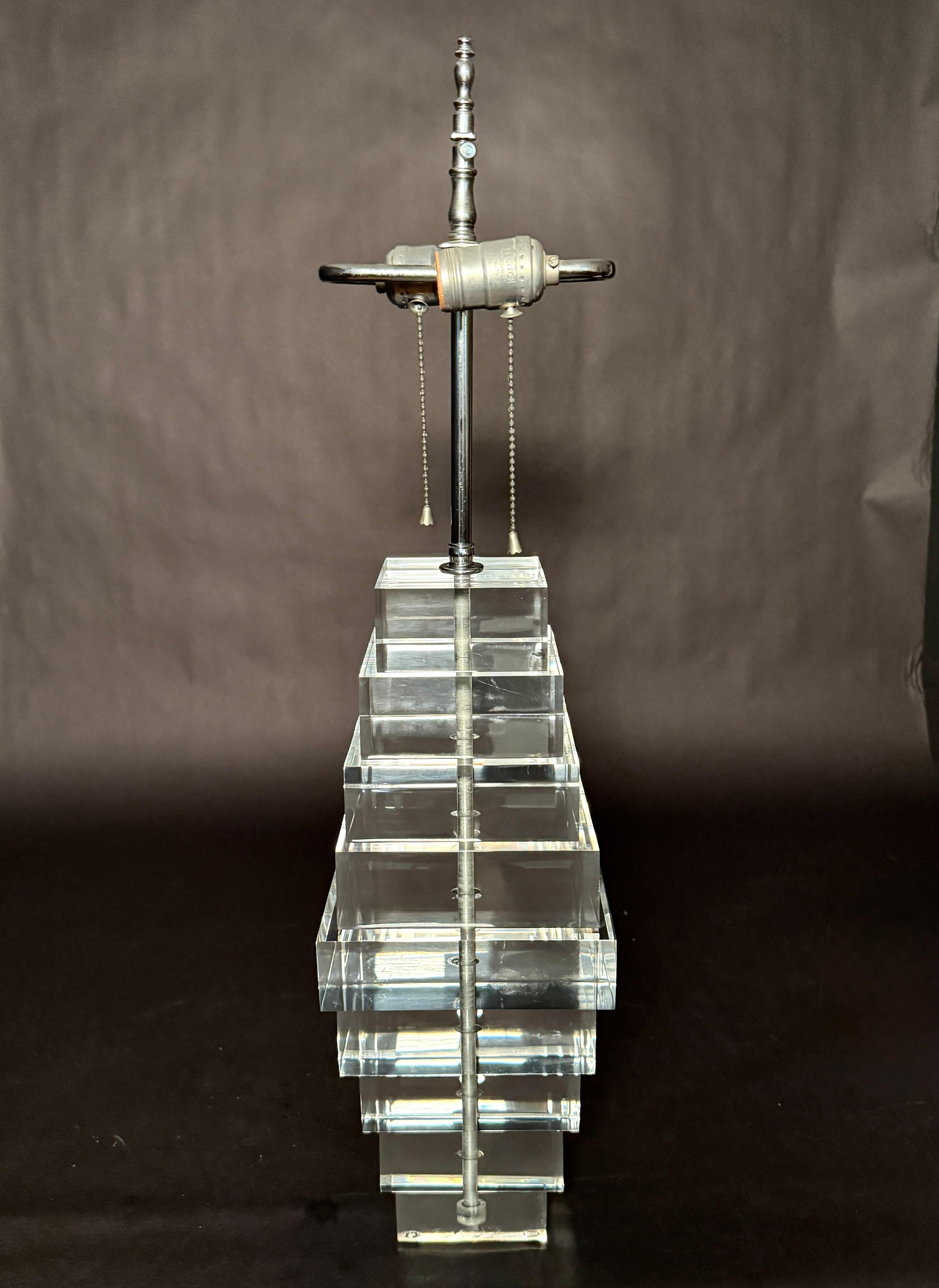 Una llamativa y escultural lámpara de sobremesa compuesta por bloques de Lucite apilados y dispuestos en forma de zigurat escalonado. La silueta escalonada evoca el modernismo arquitectónico con un guiño al renacimiento del Art Déco, que recuerda a