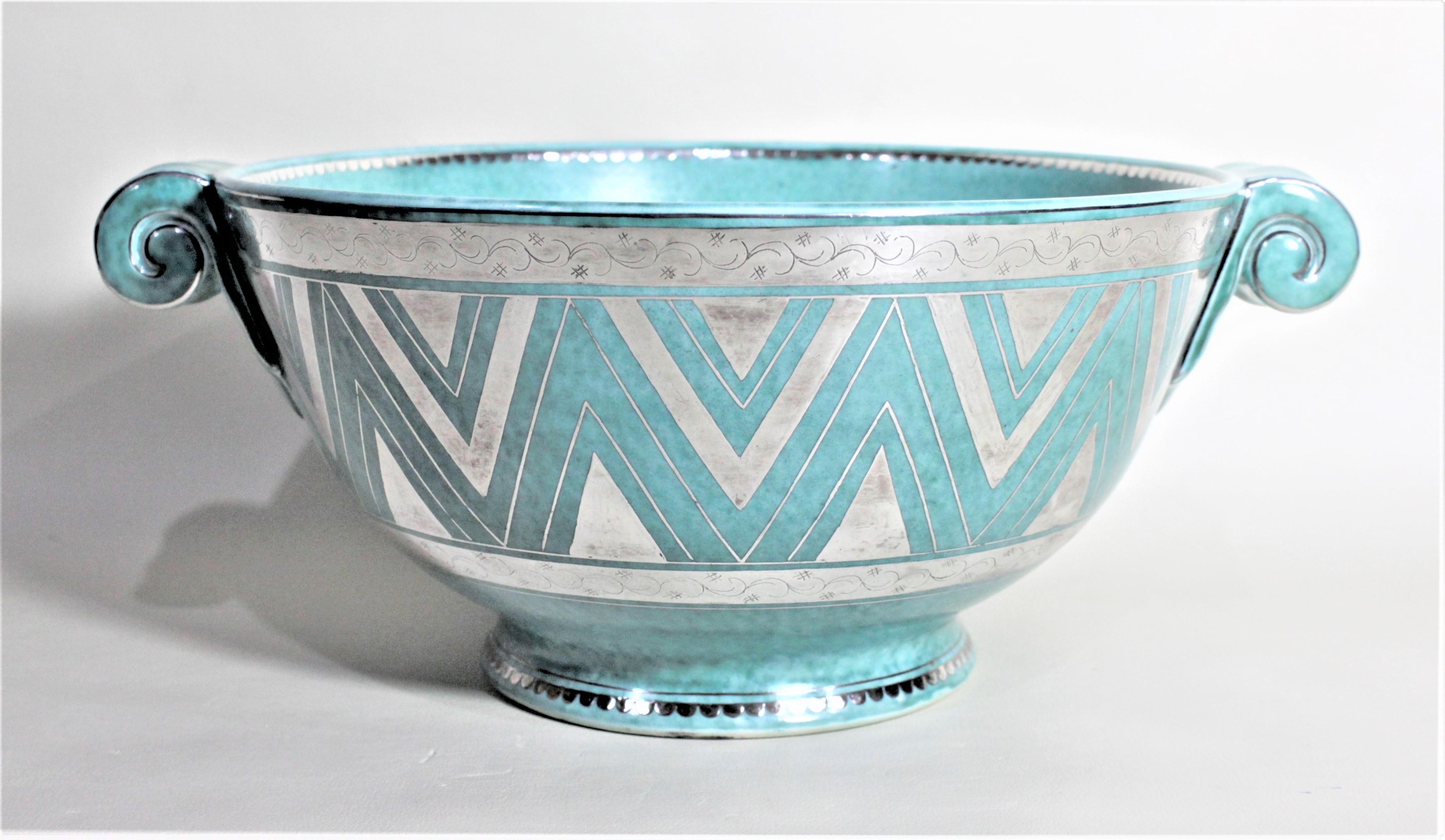 This large turquoise or 'argenta' Art Deco pottery bowl was done by Wilheim Kage for Gustavsberg of Sweden in approximately 1939. The bowl is done with scrolled handles and a pedestal base and heavily decorated with applied silver. The outside of