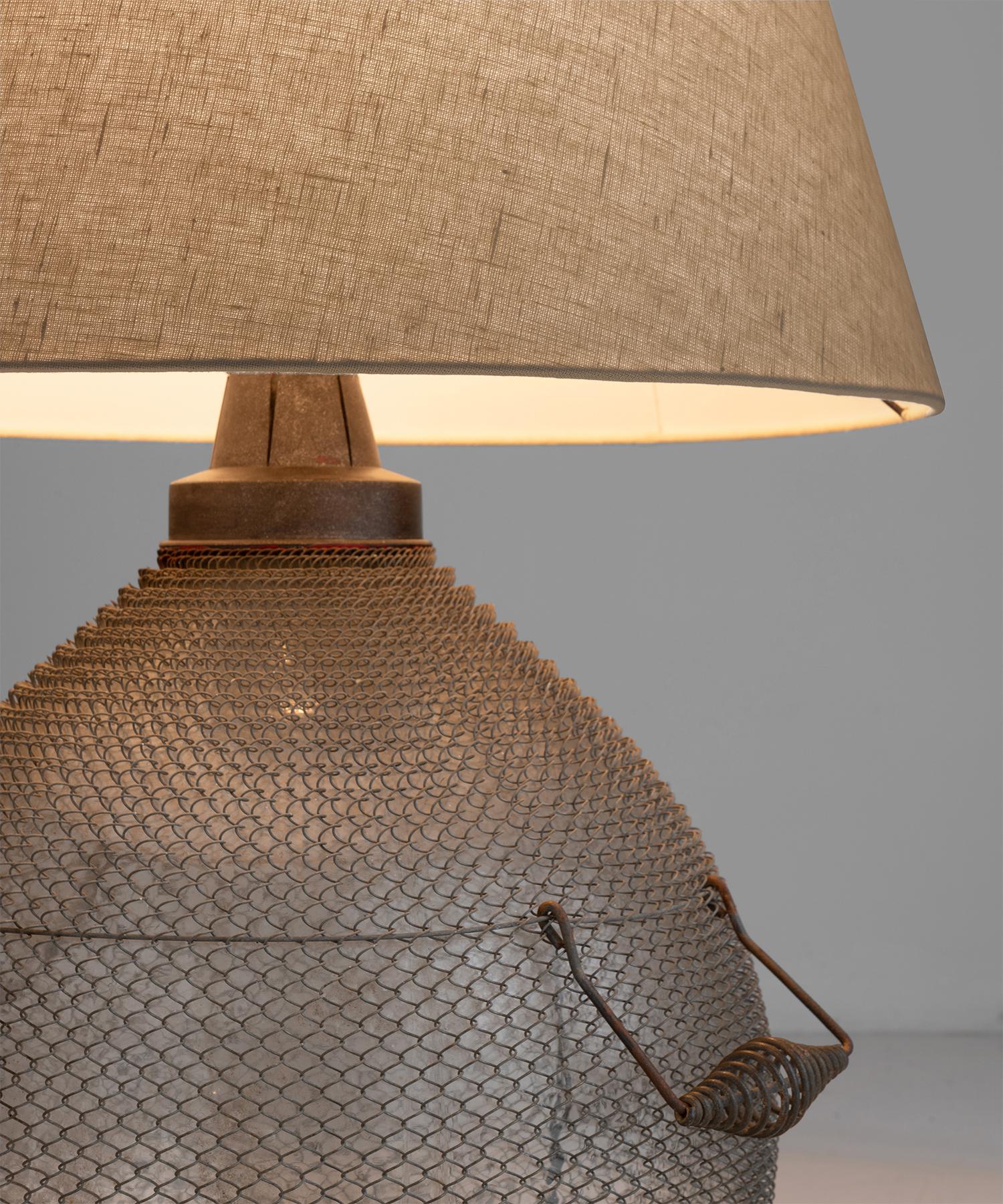 Glass carboy with wire mesh armor and carrying handles converted into table lamps.



Measures: 19.5” diameter x 29.5” height.
  