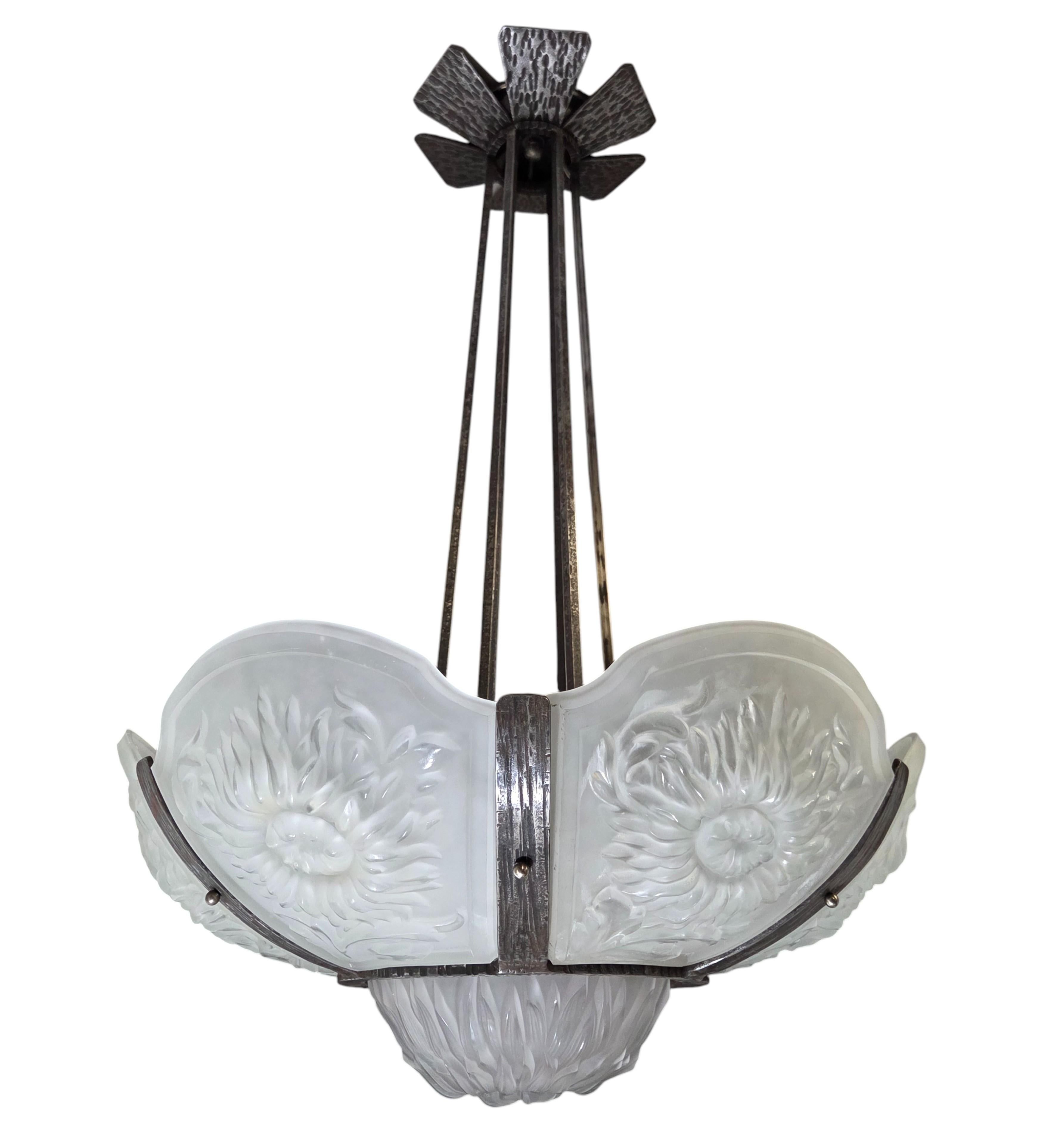 
A large and unusual original Art Deco period blossom chandelier featuring six bulbous floral motif frosted art glass panels sand a small central coupe in the original hand hammered iron frame featuring a six bar stem and culminating with a matching