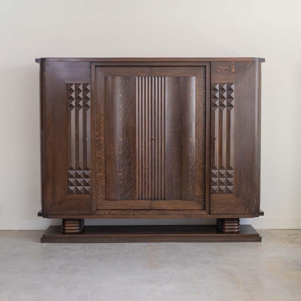 Incredible large oak cabinet by Charles Dudouyt from France, 1930s. Beautiful carved wood with intricate detail on four front doors. Three compartments open to original adjustable shelving. Original brass hardware with three keys. Cabinet rests on a