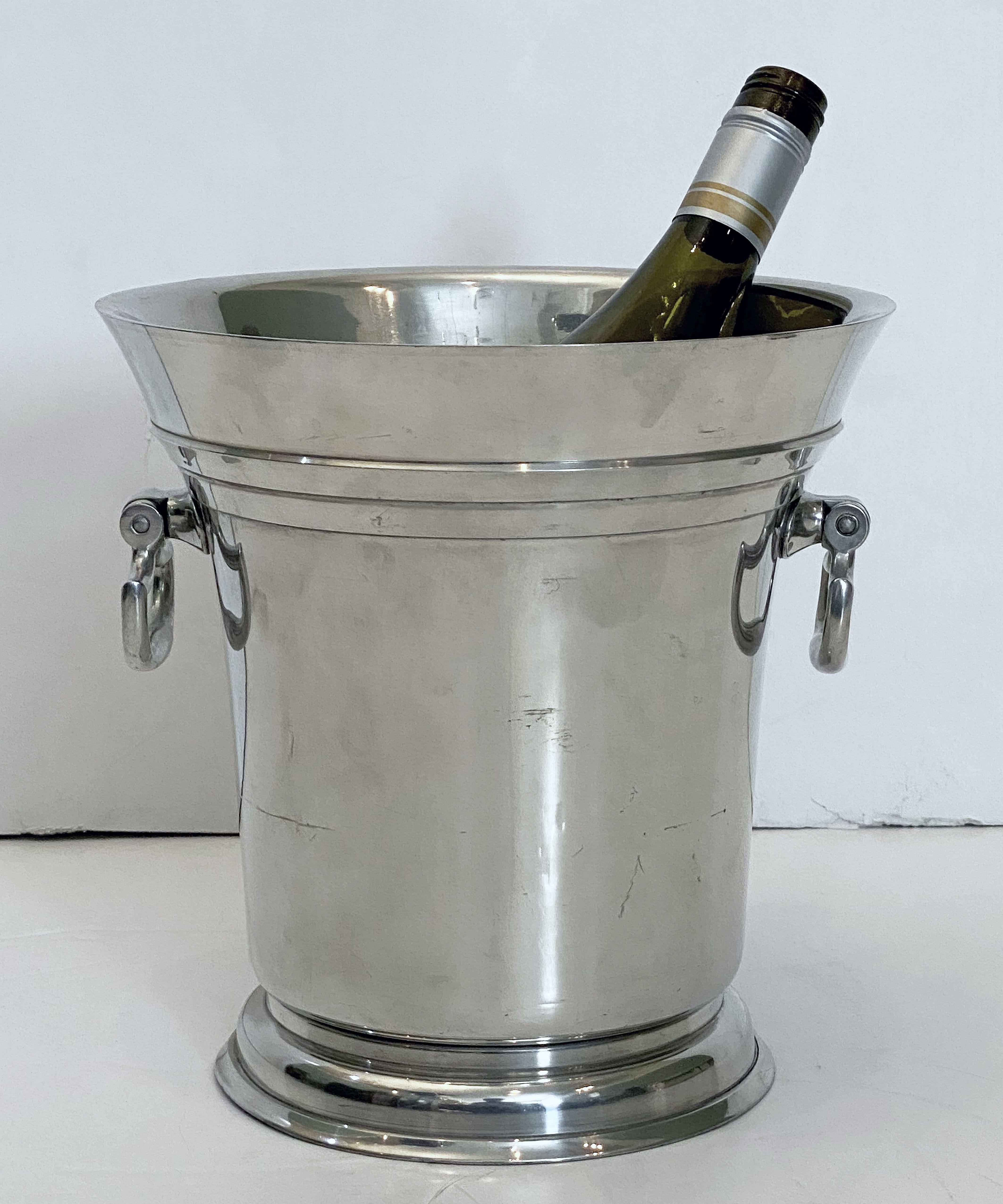 A large French champagne bucket in the Art Deco style, of a fine polished silver metal known as Etain alloy pewter, featuring a flared edge, opposing handles, and a raised platform base.