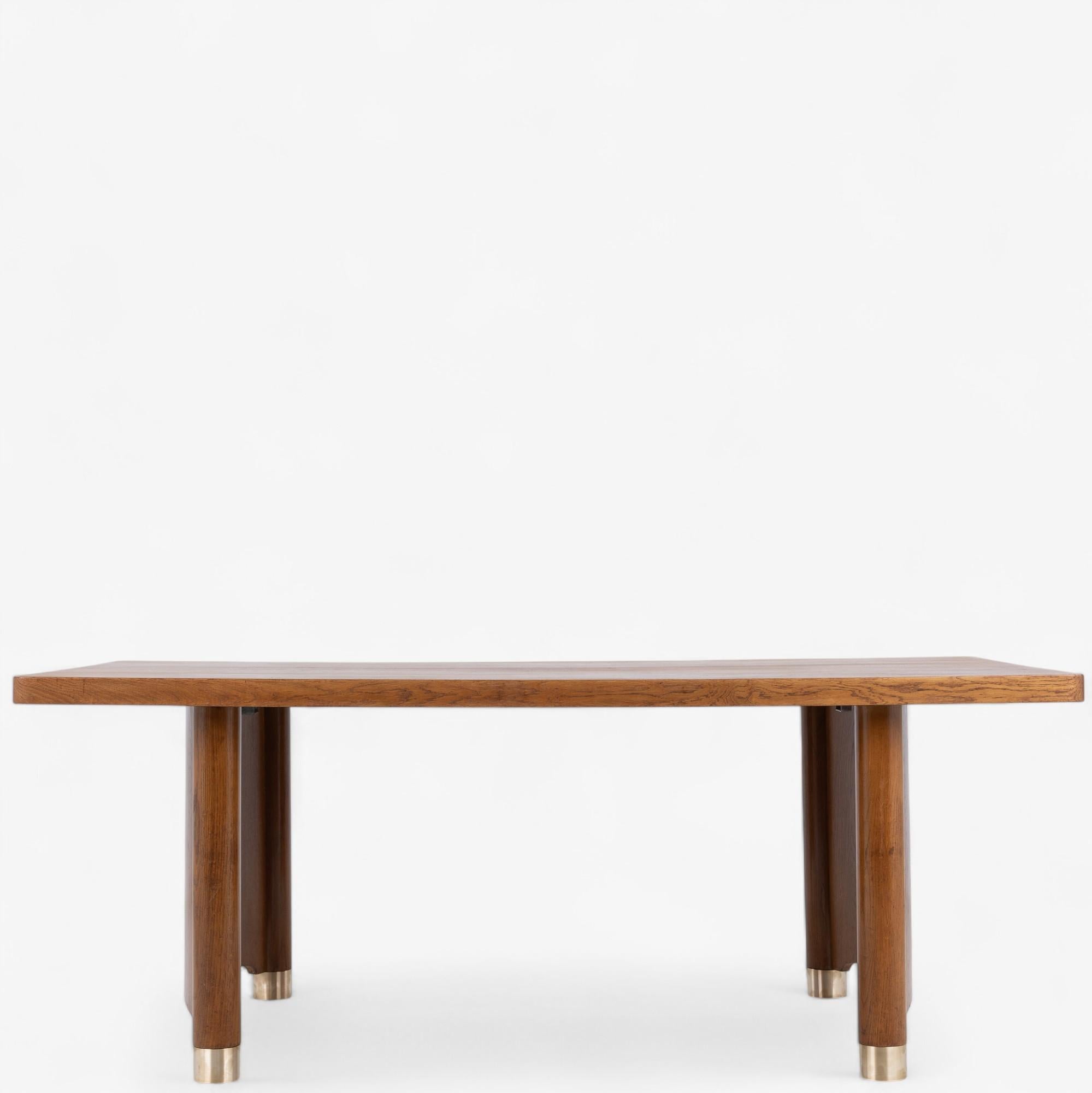 Large 'Art Deco' dining table/desk in patinated oak with curved column legs and brass shoes. From the 1930s.
