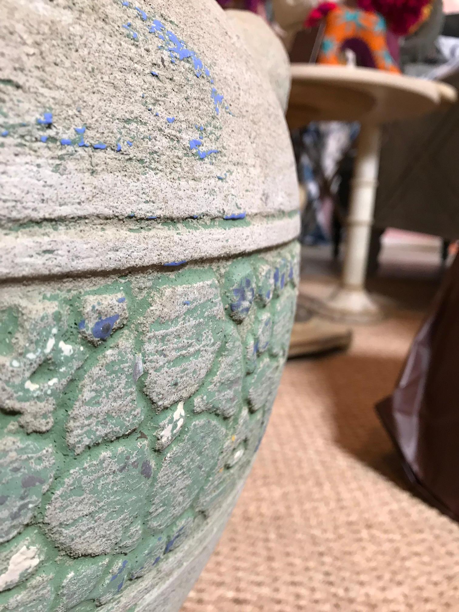 This pot is made from a hard porous, rock-like material. It has a section wrapped around it with decoratively pieced-together flower engravings. The section is a light leafy green strewn with spots of sky blue throughout the piece. The inside is