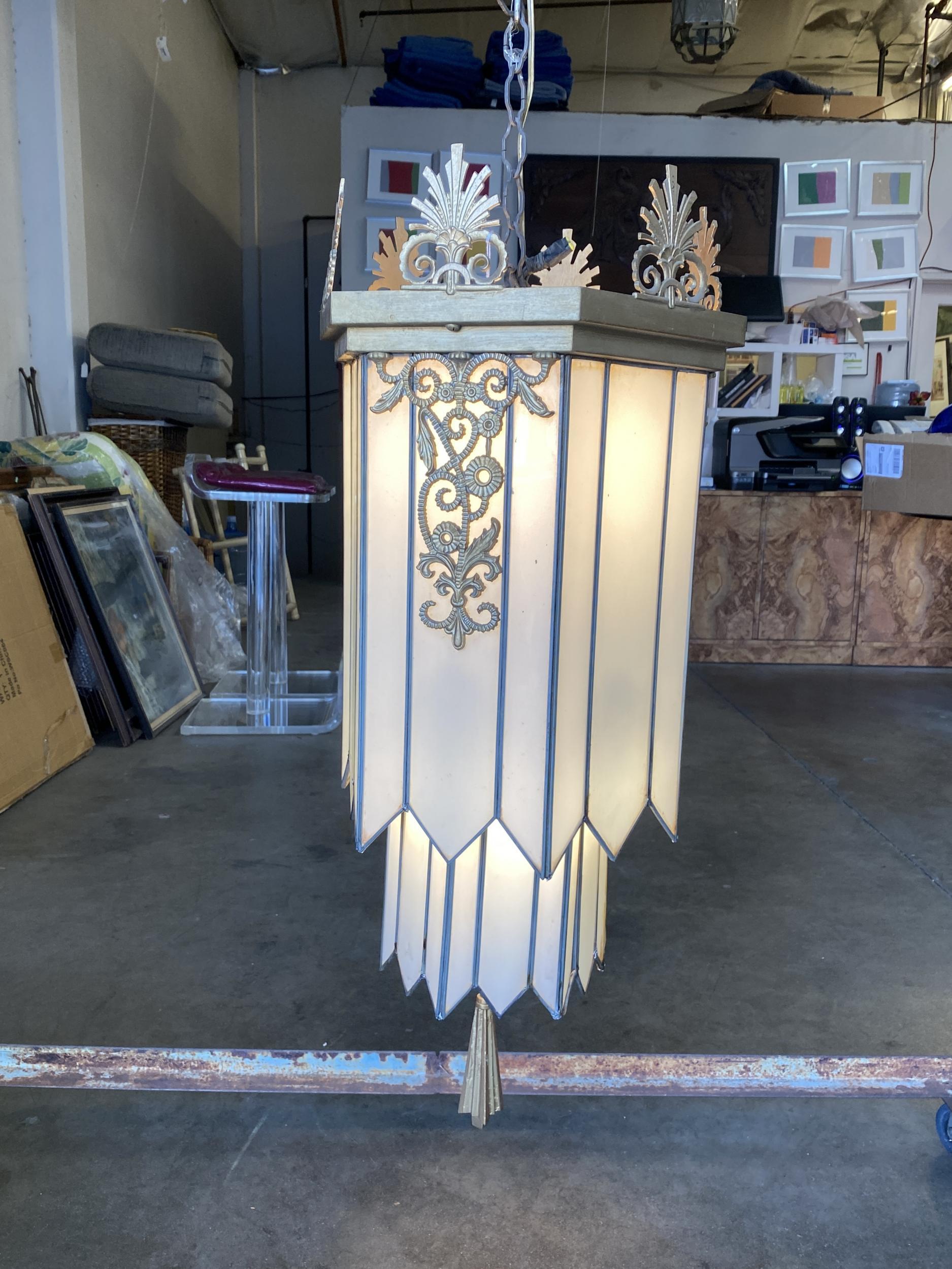 This geometrical Art Deco chandelier features milk glass leaded panels. The top is finished with sculptural scrolling motifs in bronze.
