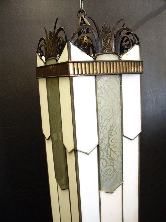 This geometrical Art Deco chandelier features both acid etched and milk glass leaded panels. The top is finished with sculptural scrolling motifs in bronze.
