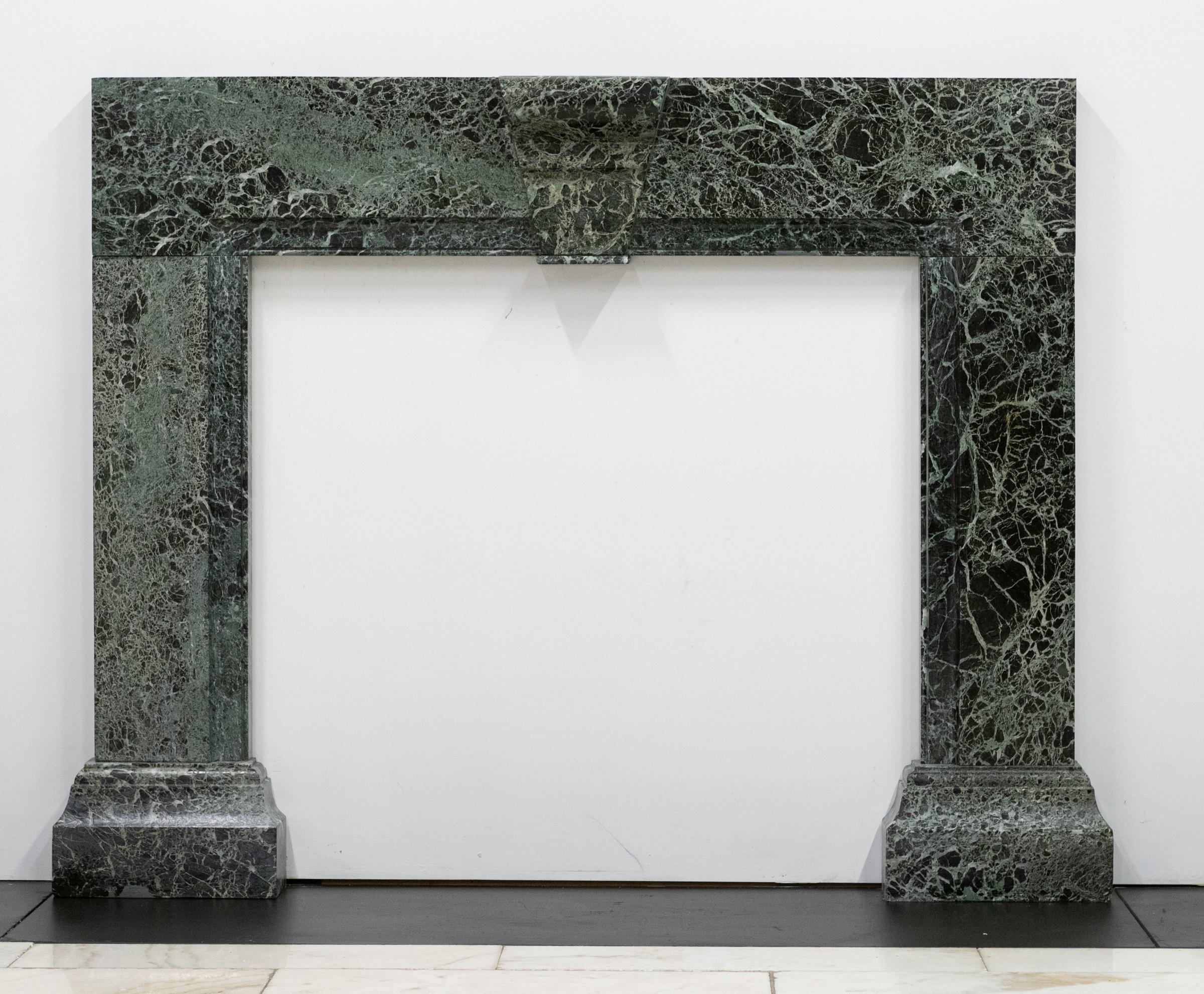 Avec un clin d'œil au style Queen Anne, cet entourage de cheminée aux proportions audacieuses est fabriqué à partir de marbre vert italien récupéré. Il présente une clé de voûte centrale sculptée et des jambages qui reposent sur des blocs de pied