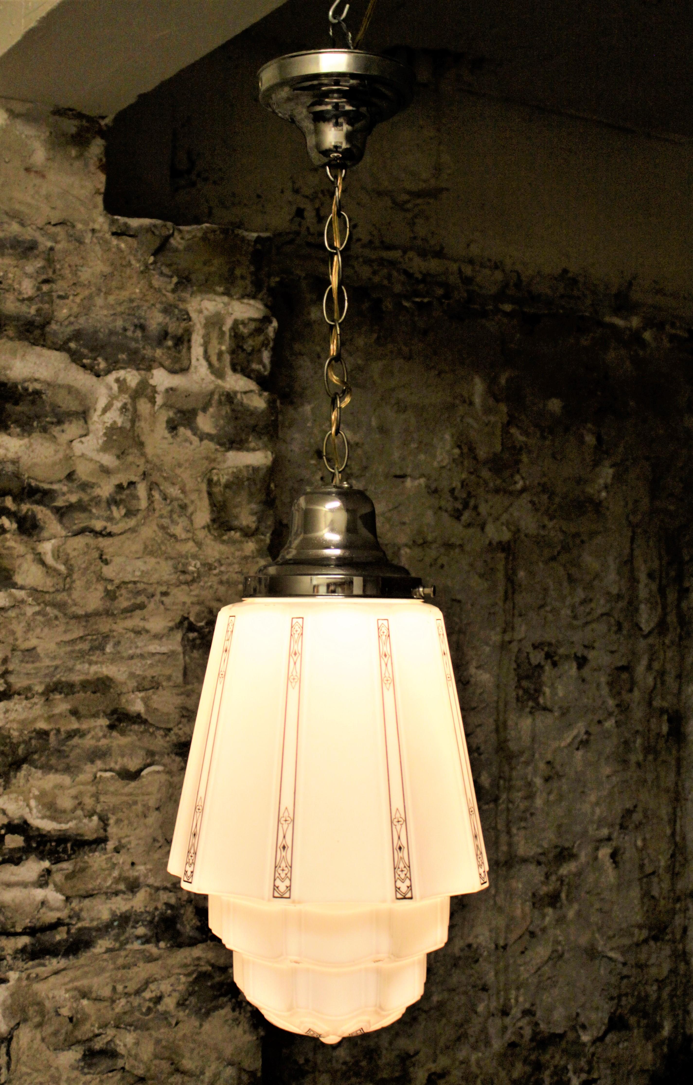 This Art Deco industrial pendant light is unsigned so the maker cannot be determined, but it is presumed to have been made in the United States in the early 1930s. The milk glass shade is done in a stepped, or 'Skyscraper' style with black geometric