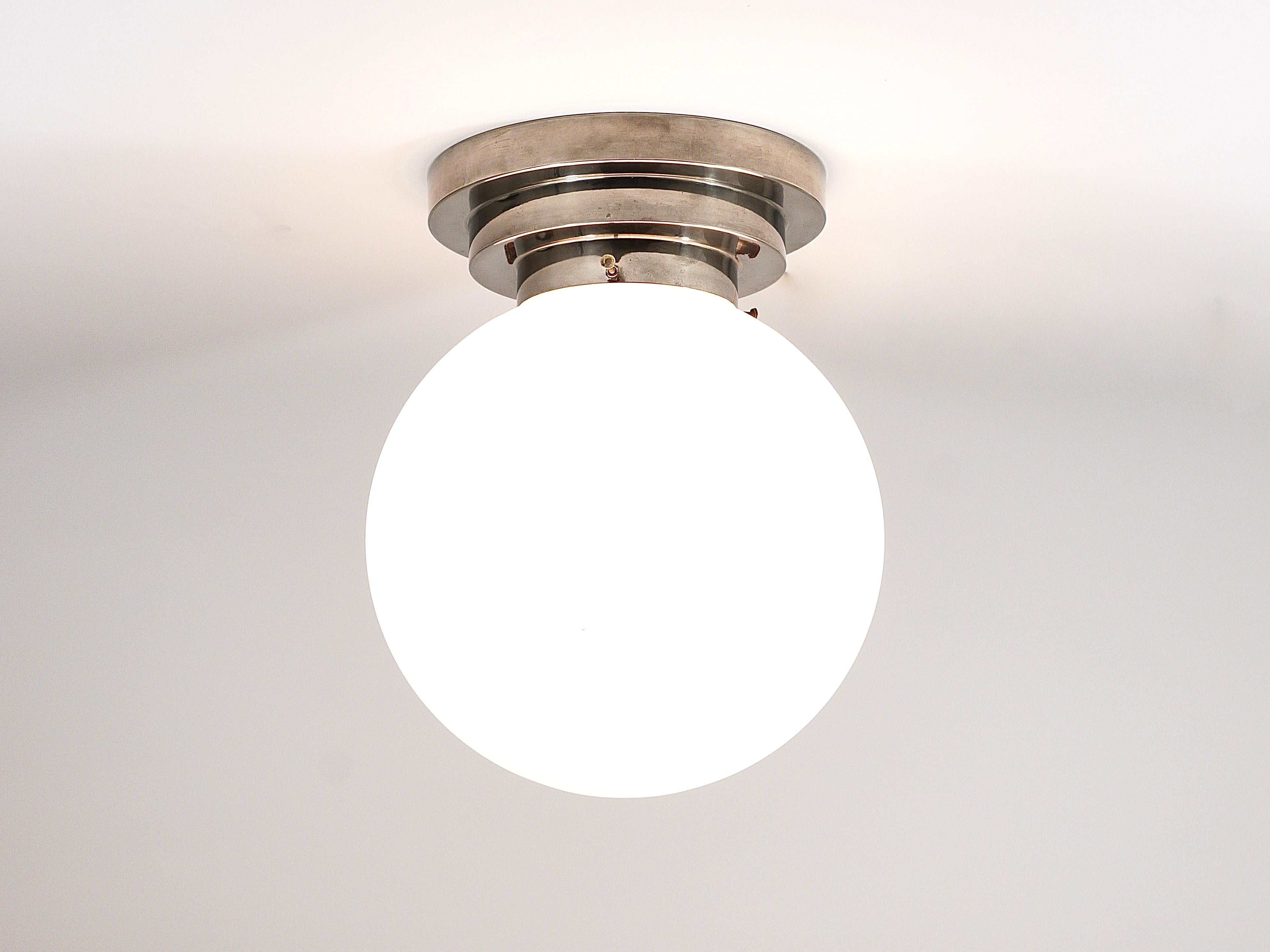 An Art Deco Bauhaus ball ceiling lamp from the 1930s, made in Germany. The light features a stepped round mount made of nickel-plated metal and a 10 inches diameter blown spherical lampshade, crafted from white satin-finished opaline glass. The lamp