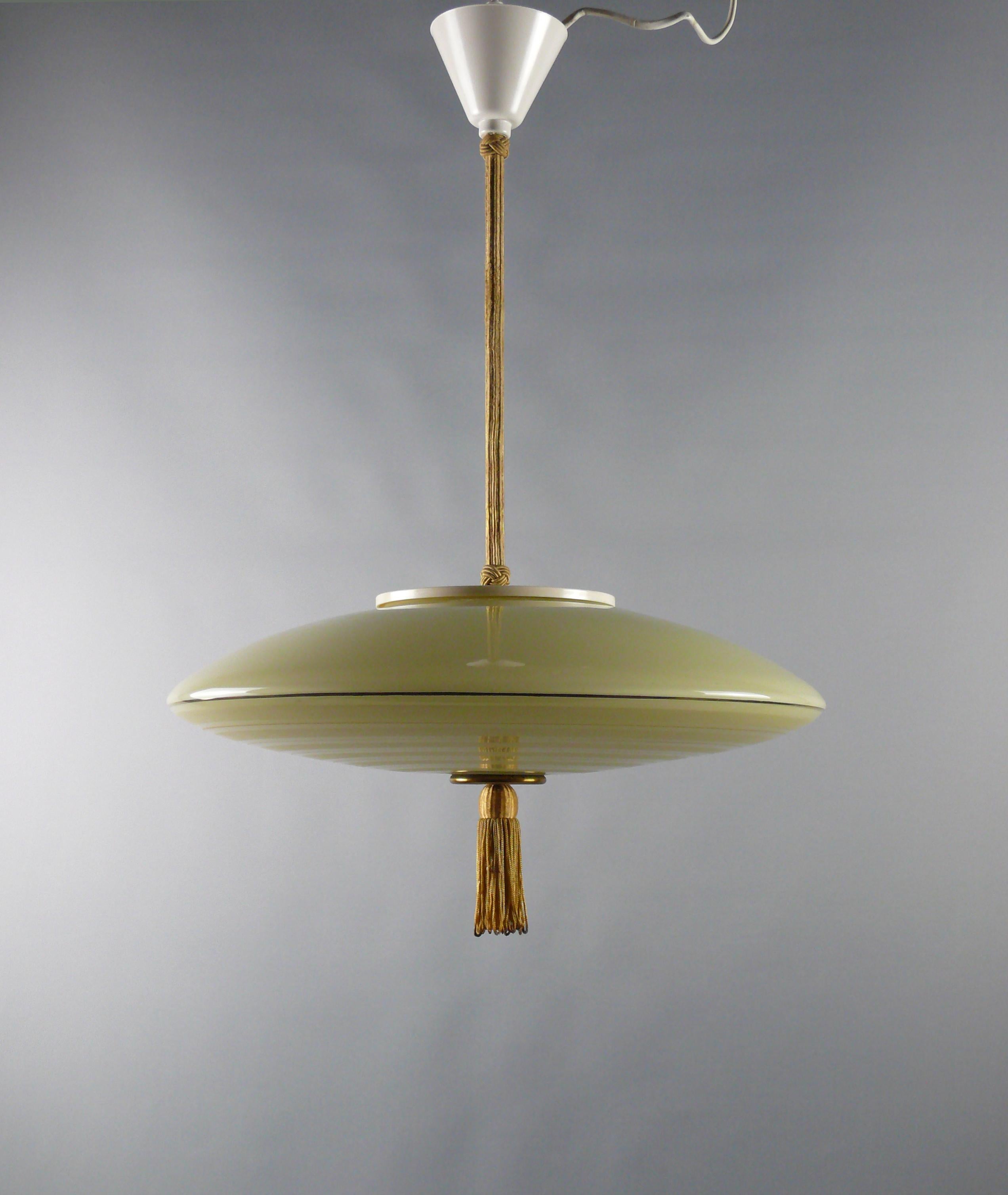 Large rod pendant light from the 1930s - 1950s with a beige glass shade, coated rod and plastic suspension.

The ufo-shaped glass shade has radial-shaped, gold-colored decorative strips and frosted areas. The lower end button is made of brass and