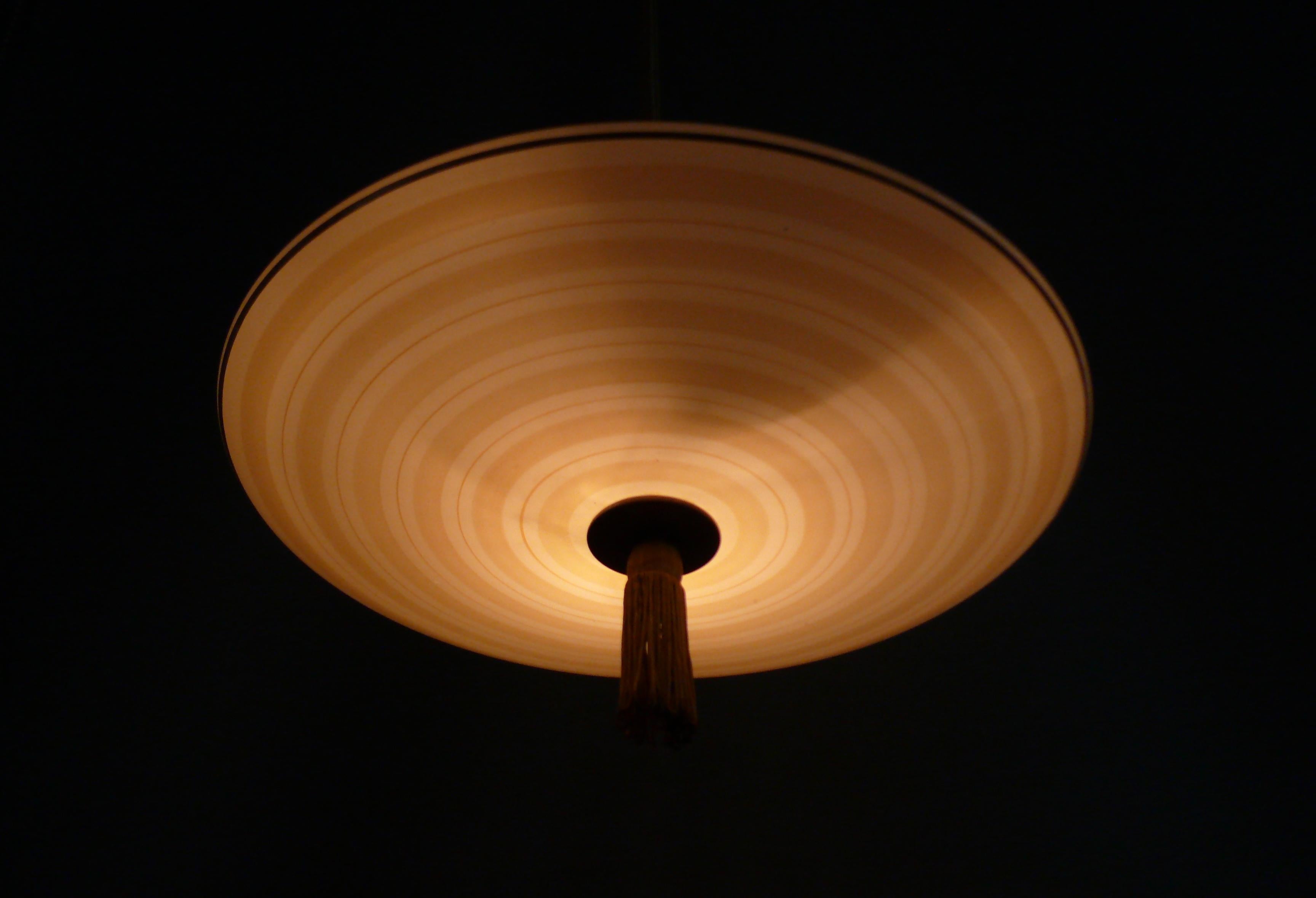 Large Art Deco pendant lamp with decorated beige glass shade from the 1930s - 1950s. The glass shade is in good condition, the golden radial stripe slightly chipped. The glass holder and canopy are made of Bakelite. The pendant rod is covered with