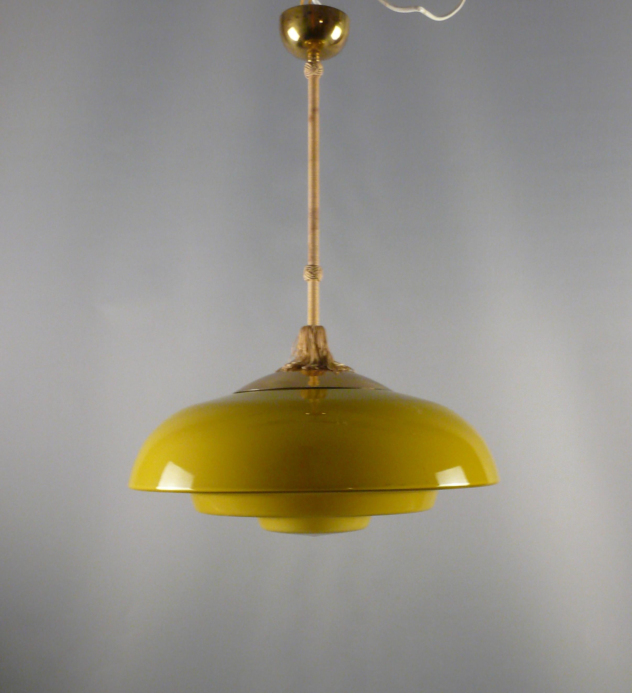 Lampe suspendue à tige Art déco jaune moutarde des années 1920-1940 avec un grand abat-jour à gradins. Abat-jour et suspension en bon état d'origine*.

L'abat-jour en verre jaune est incurvé en haut et étagé en bas et est fabriqué en verre robuste.