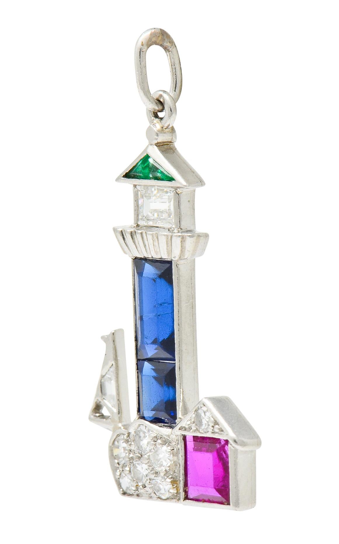 Charm designed as a lighthouse towering over a small cottage with a sailboat off the coast in the distance

Lighthouse is comprised of channel set sapphire, royal blue in color, topped by a ridged walkway and a bezel set baguette cut diamond with a