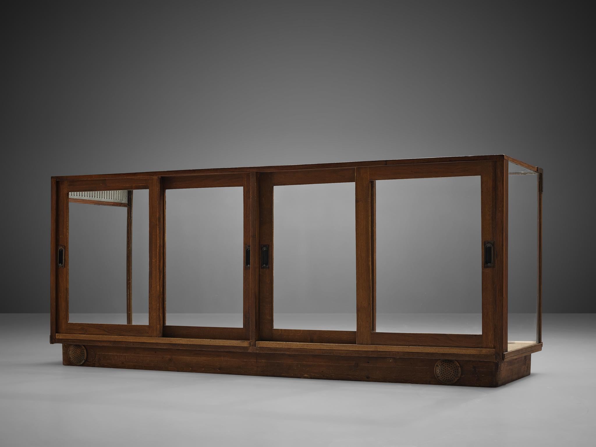 Showcase, oak, glass and metal, Europe, 1940s.

This large showcase is made in dark stained oak, with sliding glass doors and a glass top and sides. The transparency allows the user to display its personal belongings of high value such as glassware