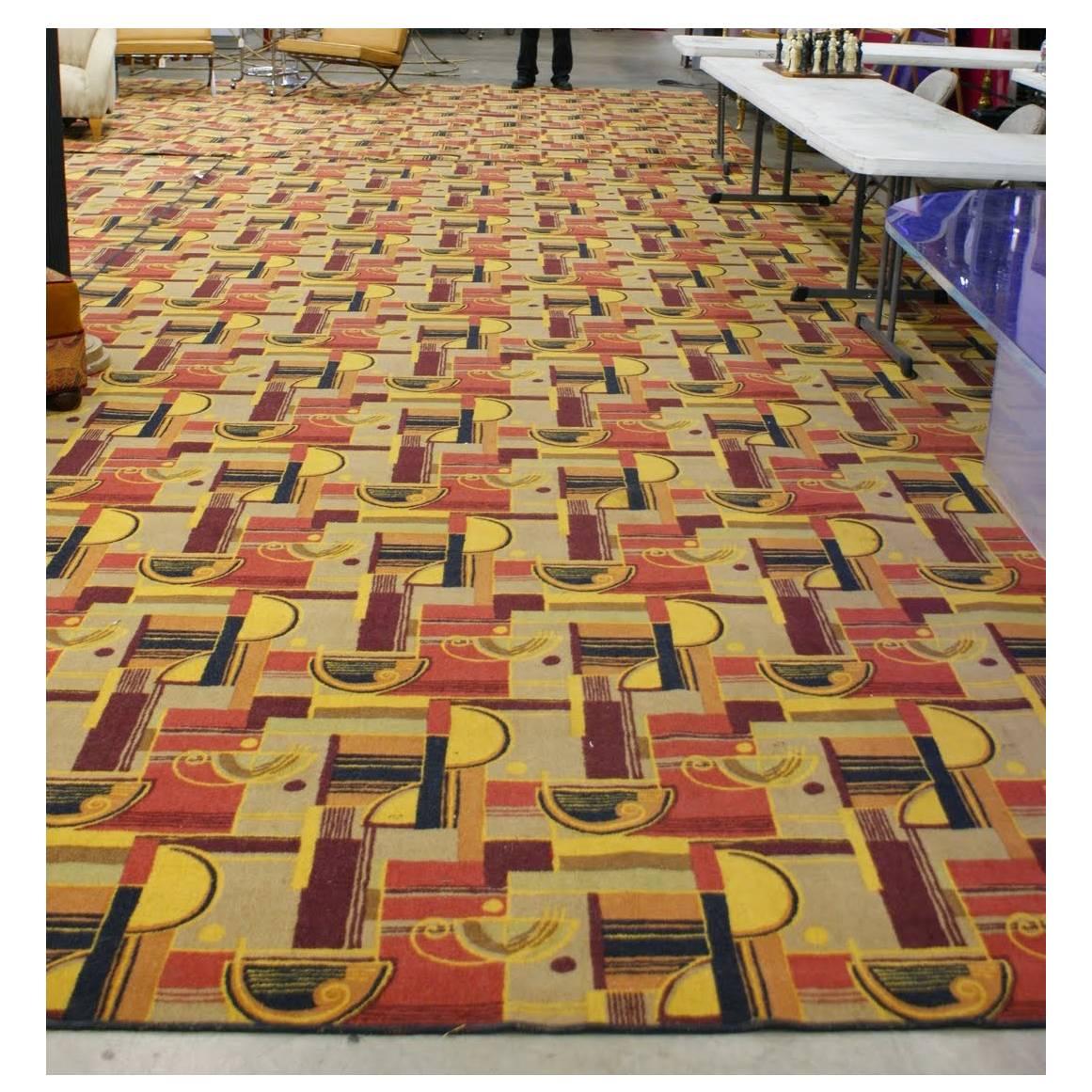 Large Art Deco style Area rug featuring a multicolored geometric streamline pattern with warm reds, browns yellows, and beige tones, much like those from Edward Fields. This rug is flooring taken from the RMS Queen Mary in the 1970s and made into a