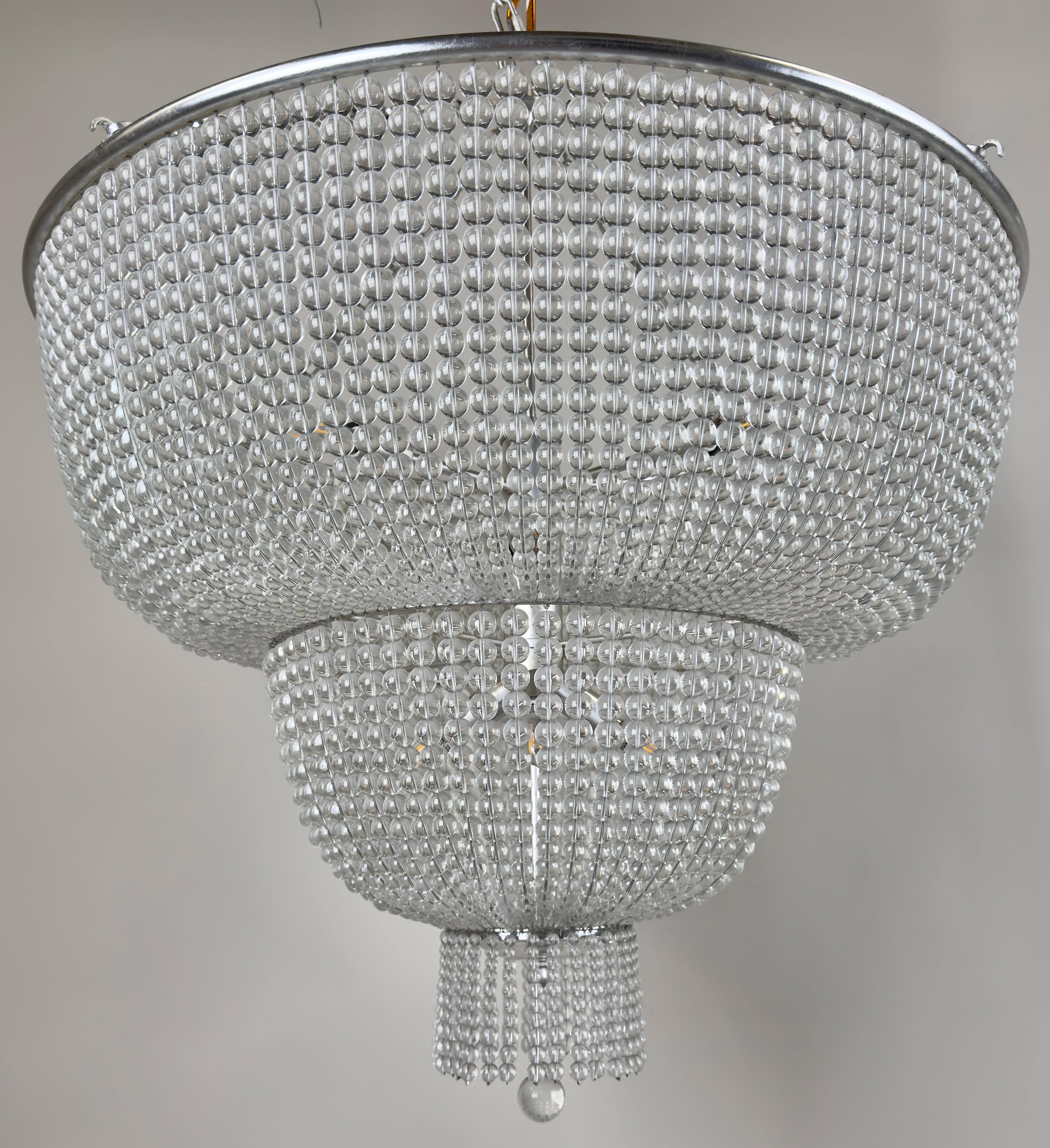 This large three-tier chandelier embodies the elegance of Art Deco design, distinguished by its refined geometry and opulent use of materials. The chandelier features a circular silhouette that tapers gracefully through three distinct tiers,
