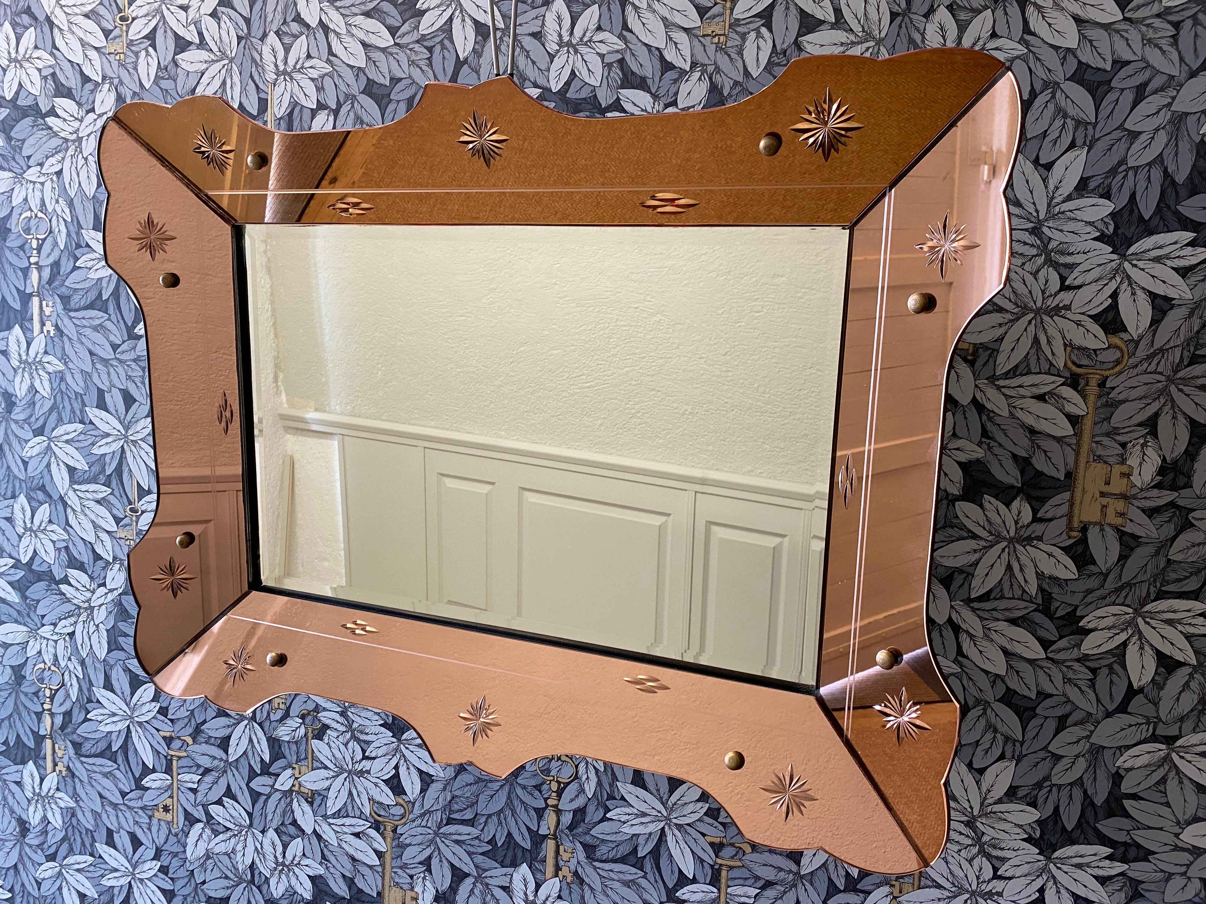 Set on a wooden back frame, the outer frame is made from decorated tinted glass and has an elegant rose gold shine to it.  

All eight screws which fix the outer frame to the back frame are covered by brass screw caps adding to the appeal of this