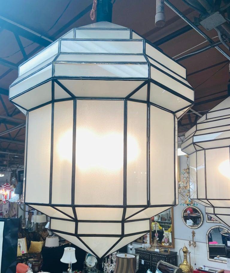 A gorgeous handcrafted pair of large Art Deco style hanging lanterns or ceiling fixtures having individual panes and featuring sandblasted frosted milky glass and patinated metal frames. The octagonal shaped large pendants have a small door on the