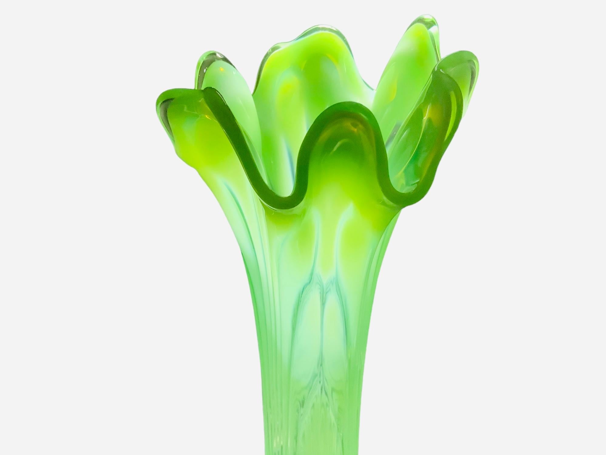 This is a large Art Glass flower vase. It depicts a transparent yellow and light apple green glass flower vase with high waves upper border. The whole vase is adorned with reeded bands that match the tips of the waves.