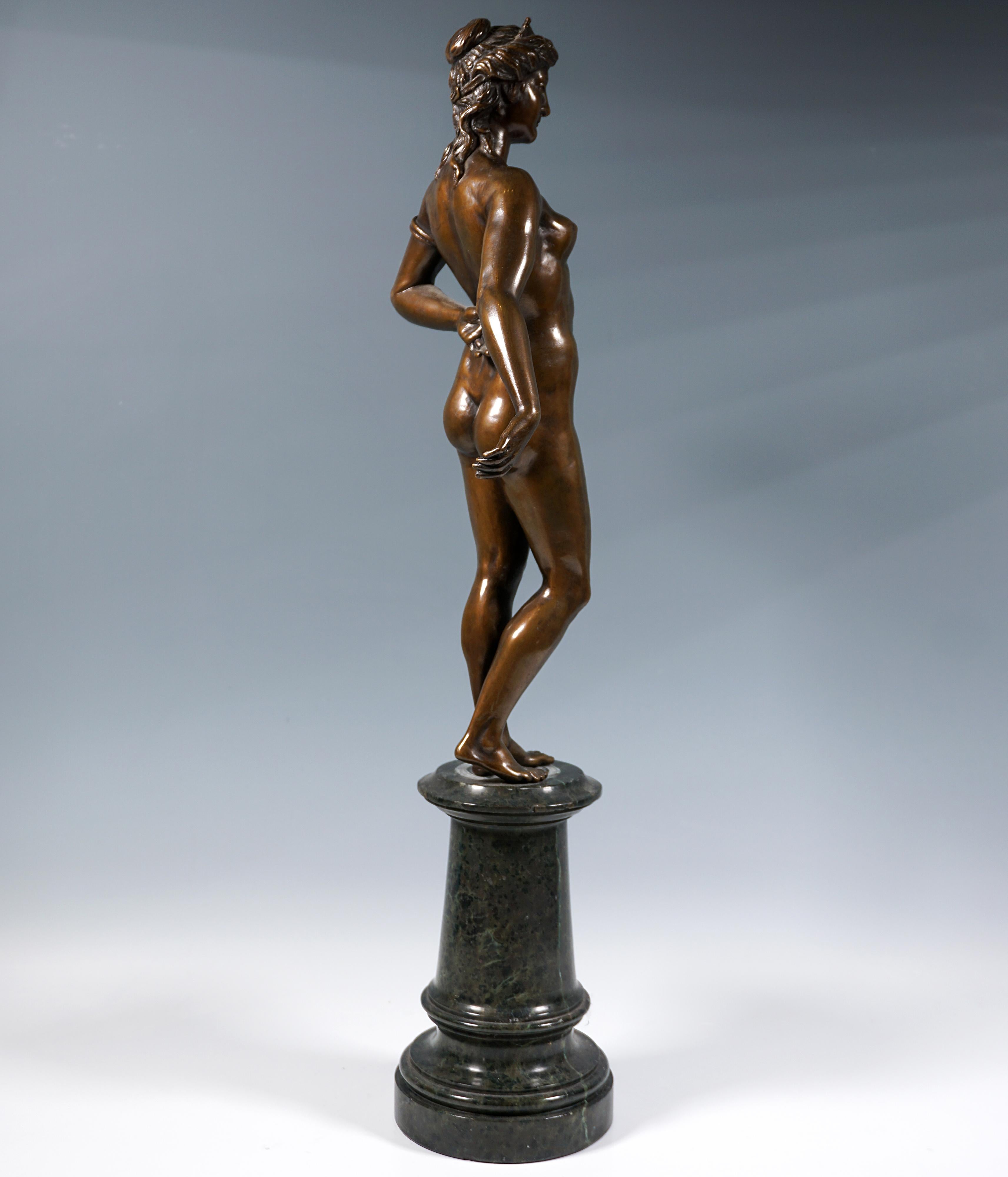 Belleza Art Nouveau desnuda, con el pelo artísticamente recogido en un nudo y cayéndole sobre el cuello, engastada con una diadema y adornada con un brazalete con estampado de serpiente en la parte superior del brazo, posando erguida con la pierna