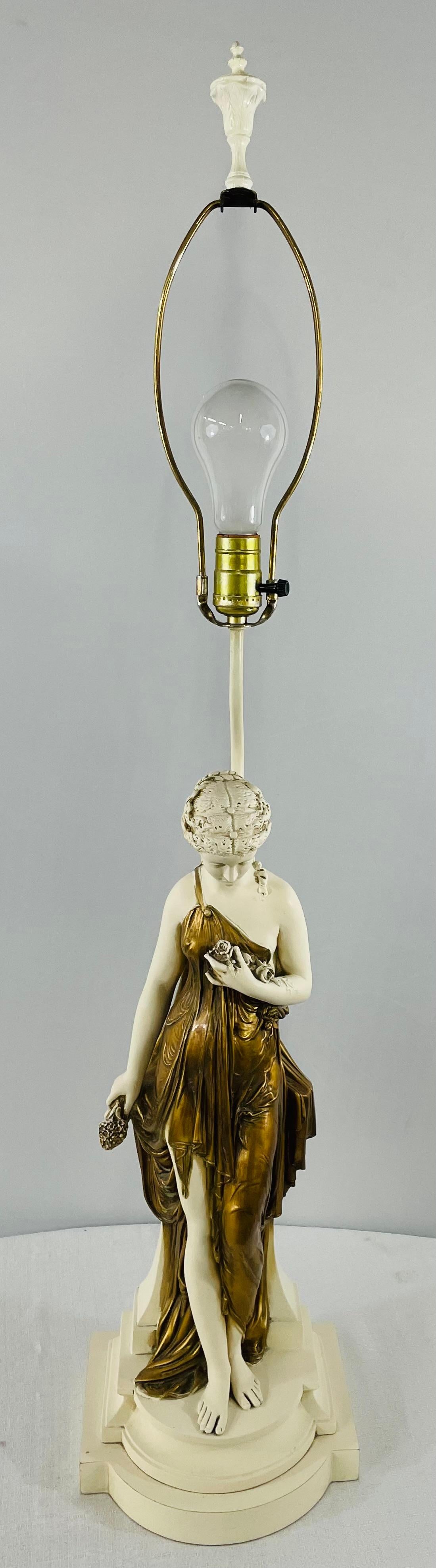 An exquisite large Art Nouveau female Nymph sculpture lamp made of porcelain. The nymph is wrapped in a gold dress and holding a bouquet of flower while looking downward. The sculpture is standing on a base signed GRANITEX on the side. Granitex is