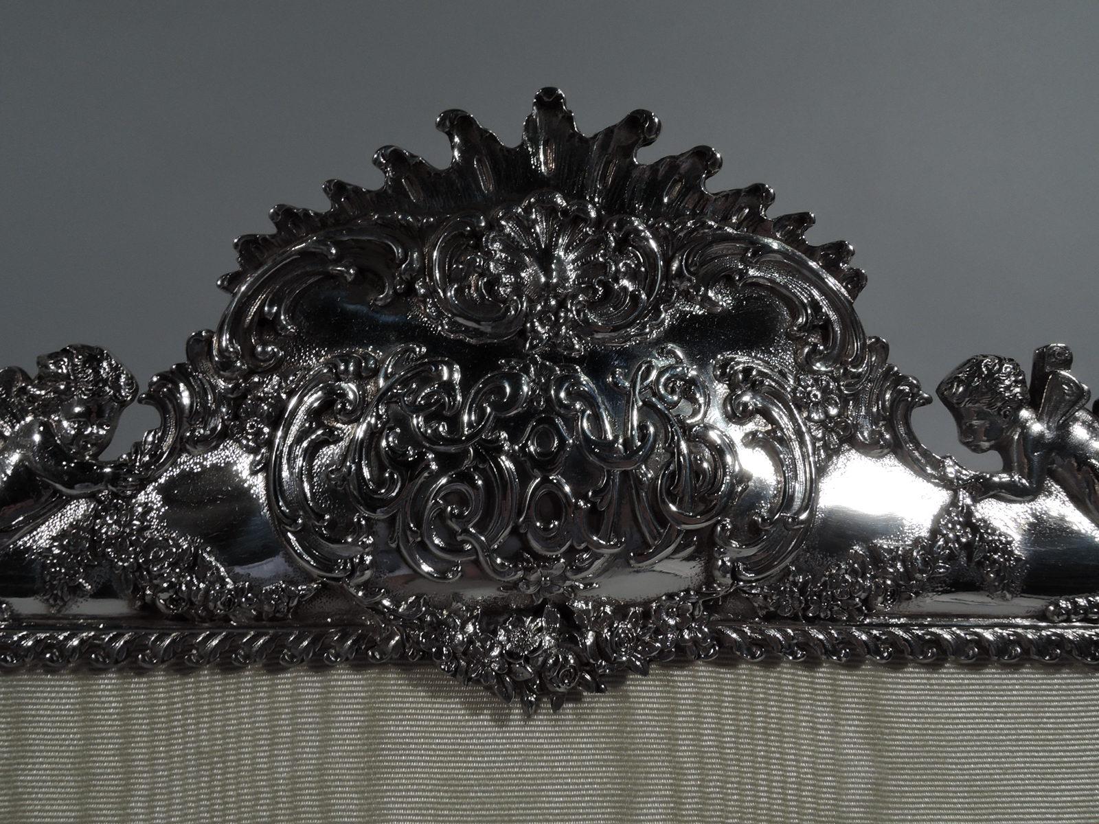 Turn-of-the-century Rococo sterling silver picture frame. Made by Tiffany & Co. in New York. Rectangular window and shaped ornate surround with bracket supports. At top are crown and corners with shell fans, winged putti supporting a garland that