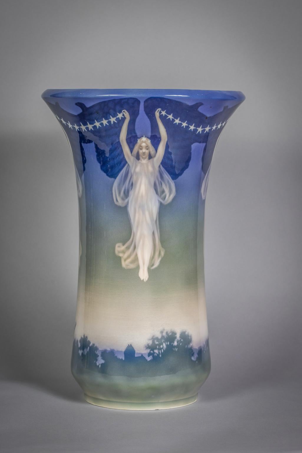 Il vaso cilindrico con bordo a forma di tromba estroflesso, decorato con mulini a vento in un paesaggio intorno alla base, ulteriormente decorato con un fregio di fanciulle vestite diafanamente che portano in alto faraglioni di stelle con