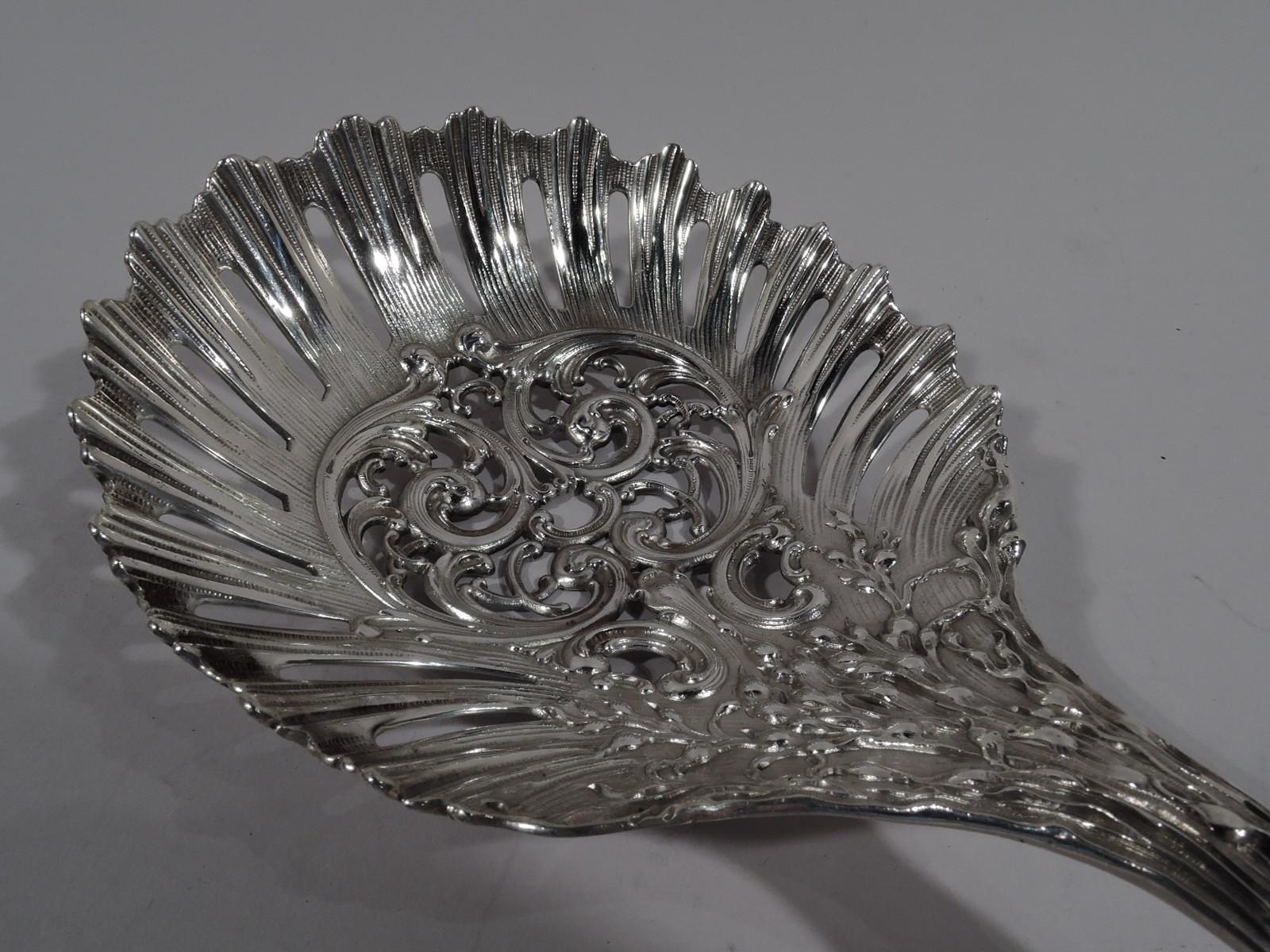 Turn-of-the-century American Art Nouveau sterling silver bonbon scoop. Large and round bowl with open scrollwork bordered by pierced striation with serrated rim. Scrolled handle with dense and entwined tendrils, and traditional shell terminal.