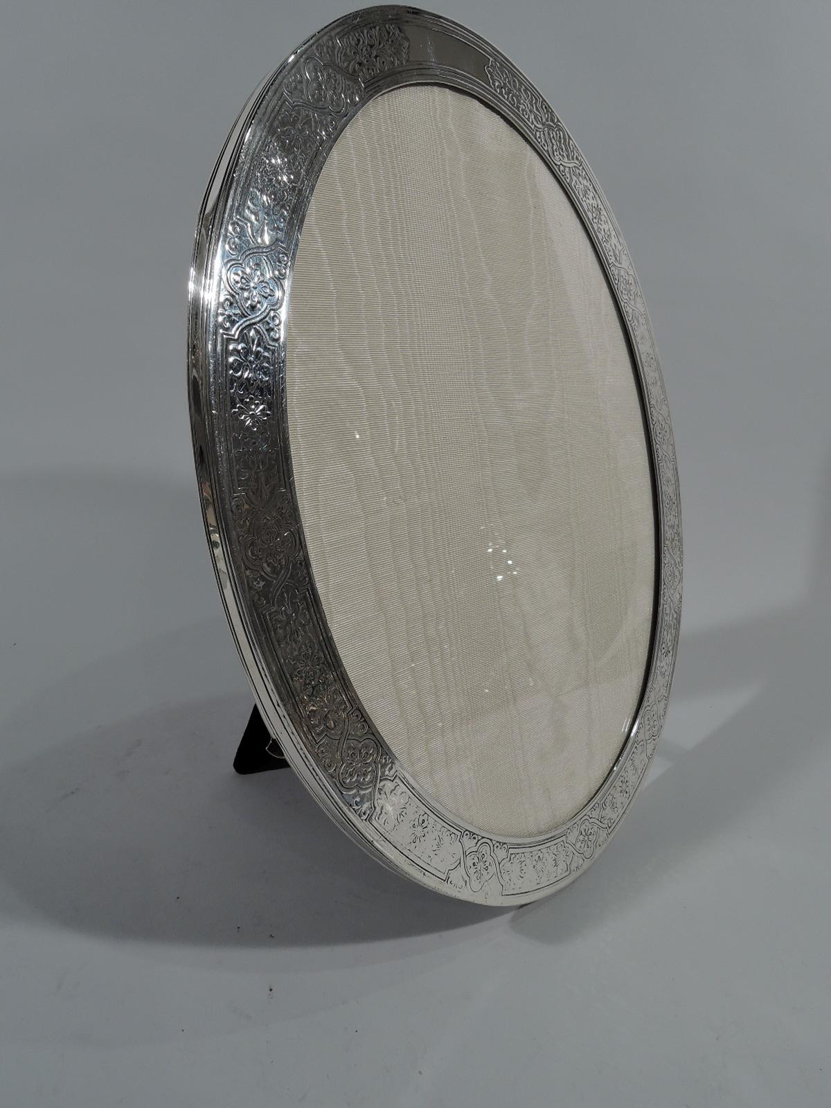 Art Nouveau sterling silver picture frame. Made by Tiffany & Co. in New York. Oval window and flat surround acid-etched with stylized flowers in curvilinear frames. Shaped cartouche (vacant). Sides have incised bands. With glass, silk lining, and