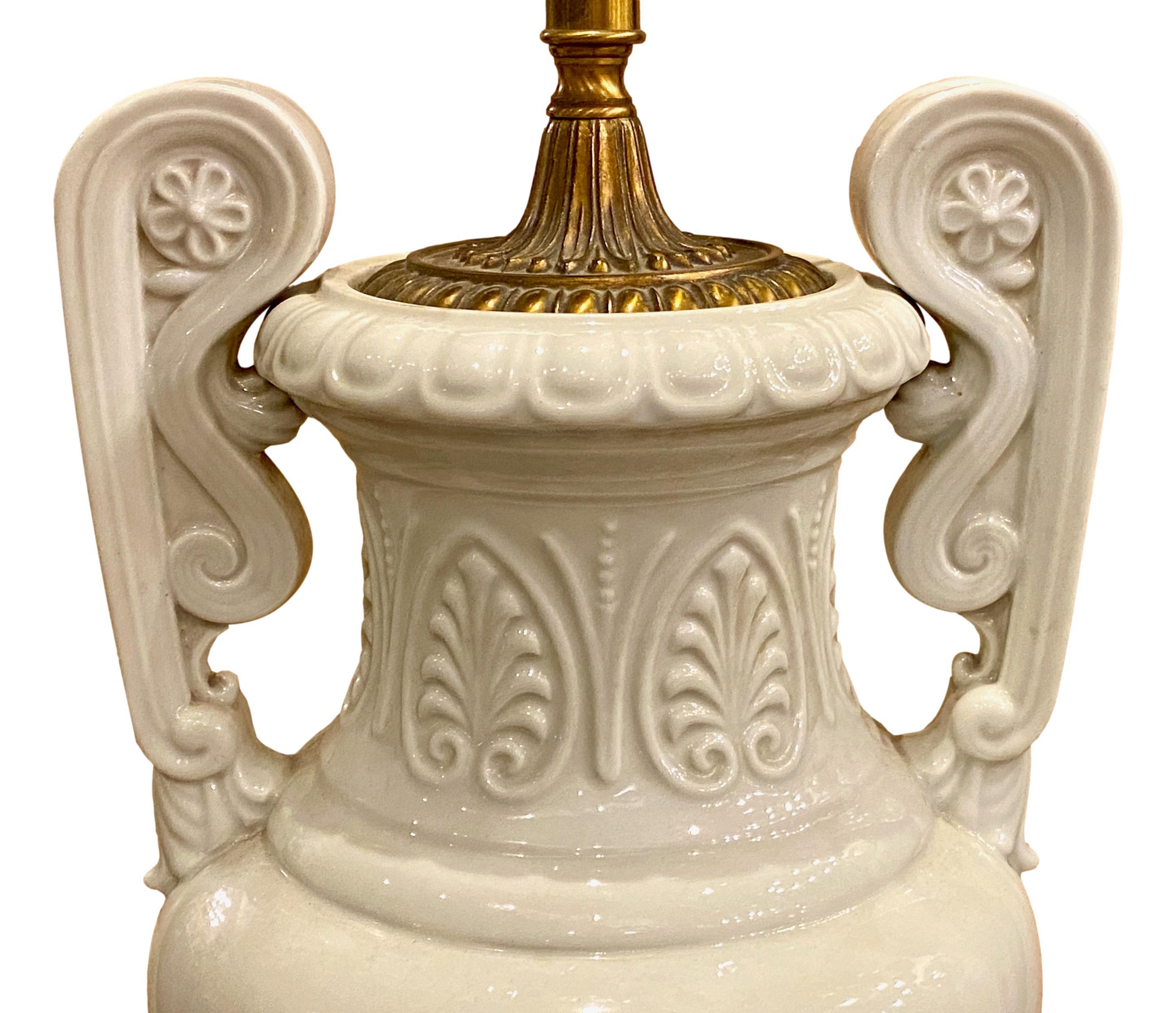 A large circa 1920's French Art Nouveau style white porcelain urn-shaped table lamp with mask and foliage details in relief on body and pedestal base.

Measurements:
Height of body: 28