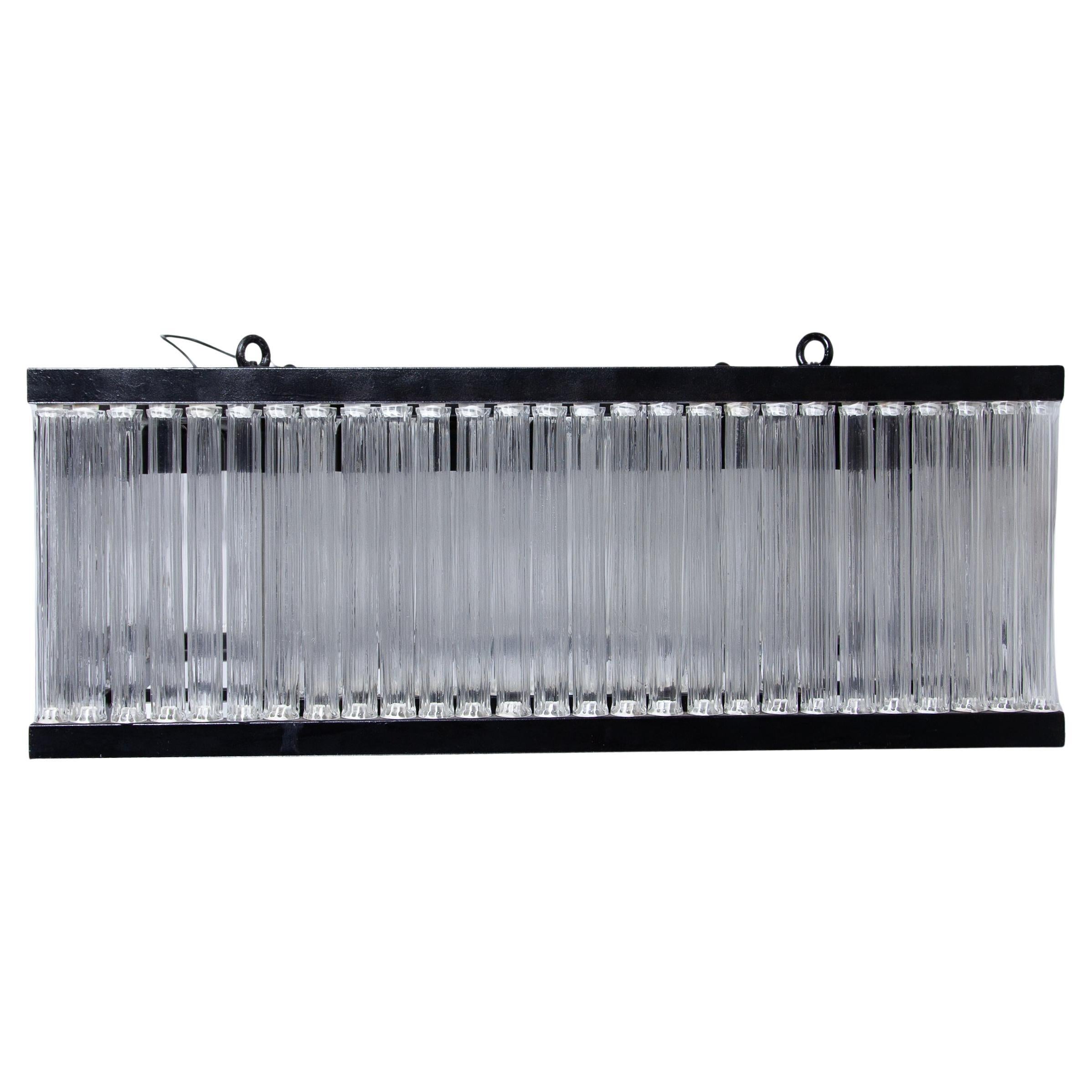 Una lampada a sospensione di grande effetto per un ingresso ampio o una stanza spaziosa. Il design del ciondolo, composto da due file di aste di vetro rigate in una cornice quadrata di metallo rivestito di nero e da 9 punti luce su ciascun lato,