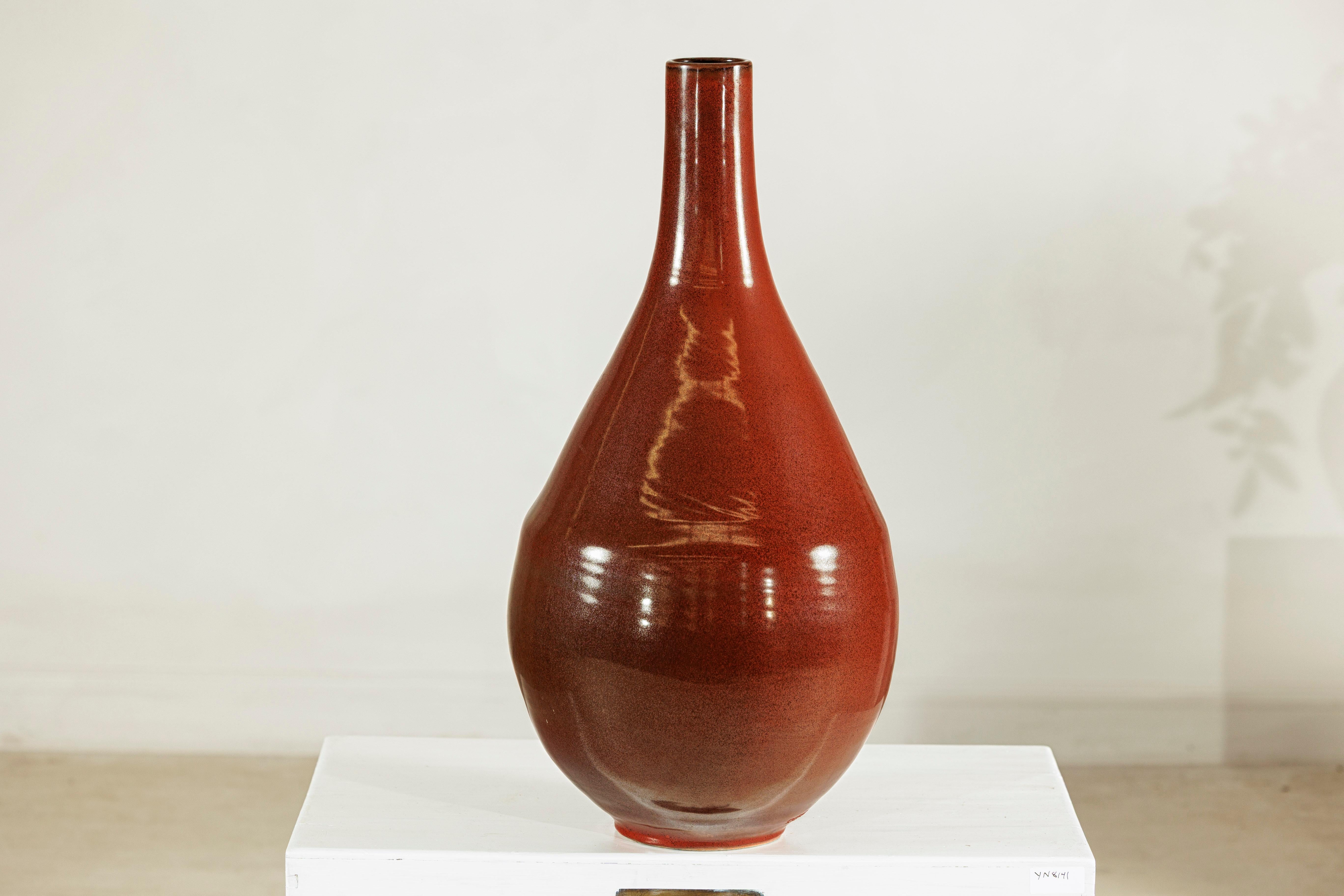 Ce grand vase artisanal en céramique présente une élégante forme de goutte d'eau avec un col élancé et une base arrondie. Fini dans une glaçure brun foncé uniforme avec une surface lustrée et brillante, le vase reflète magnifiquement la lumière à